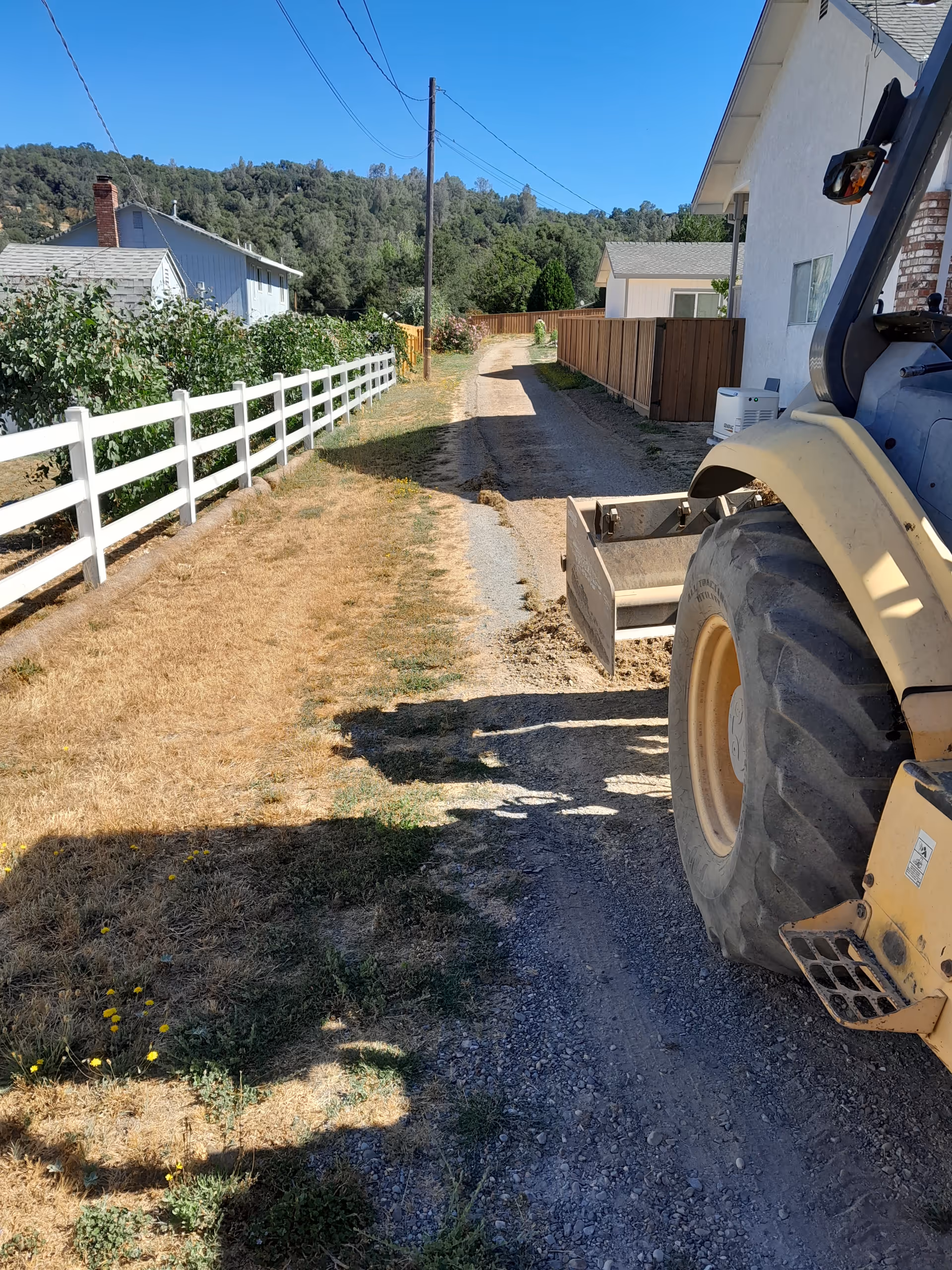 Gravel driveway beside a white house with a large tractor on the right.