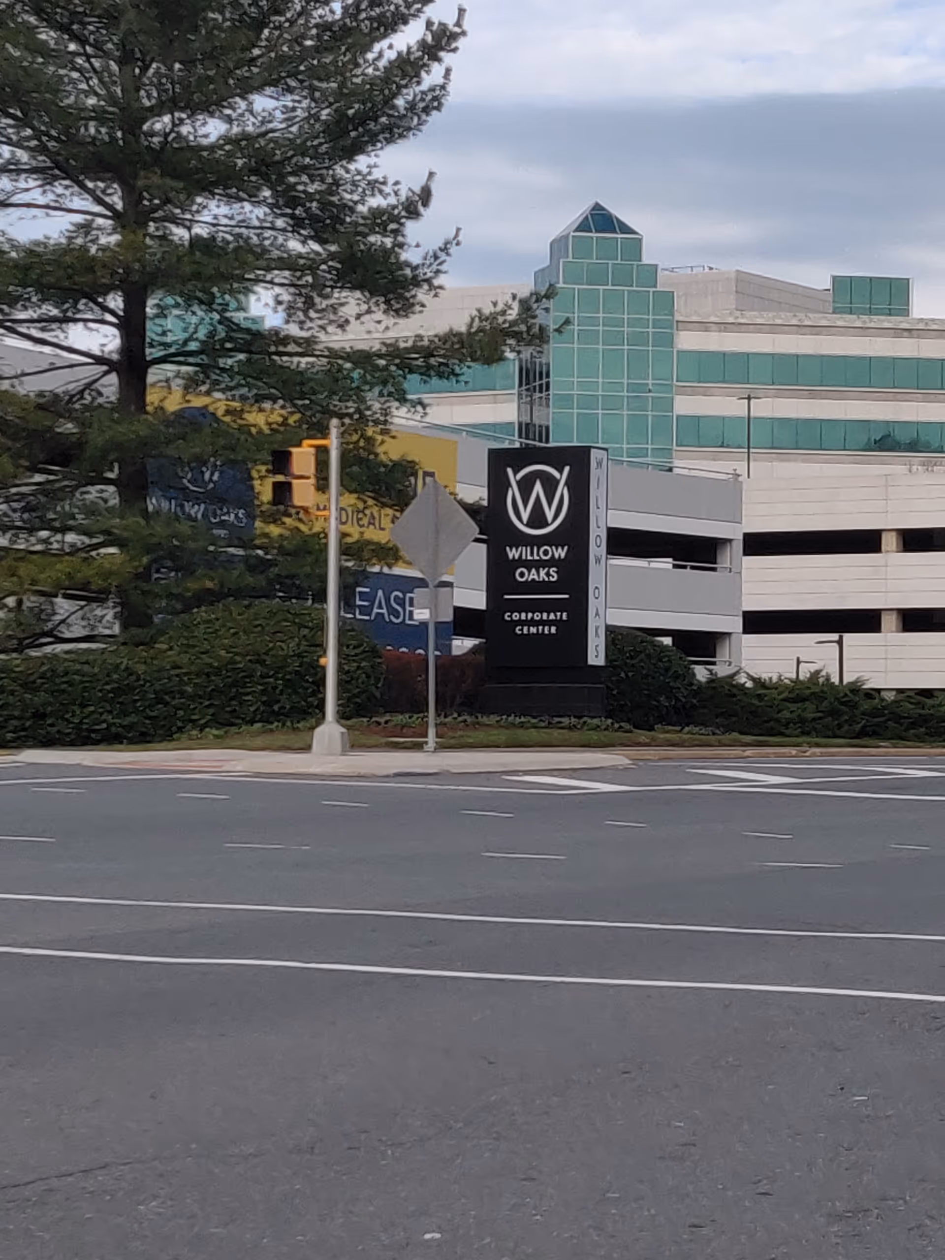 Exterior street view showing a Willow Oaks Corporate Center sign and green glass building.