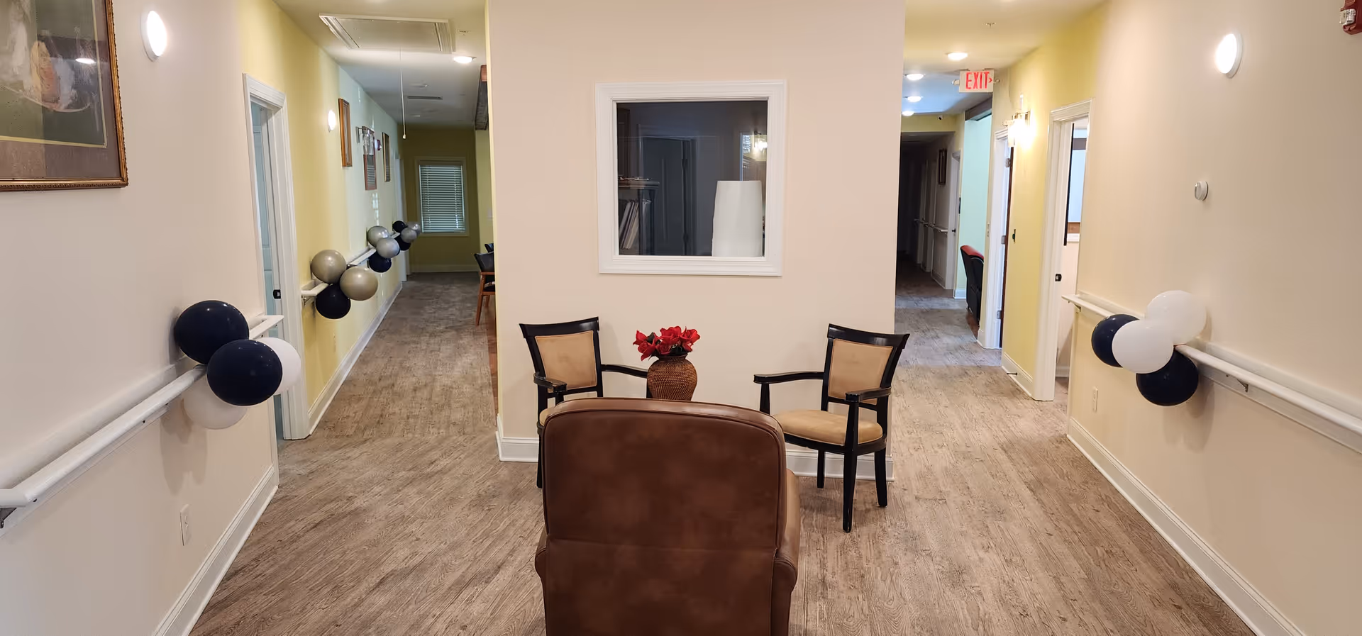 Interior hallway of a senior living facility with a seating area and balloons.