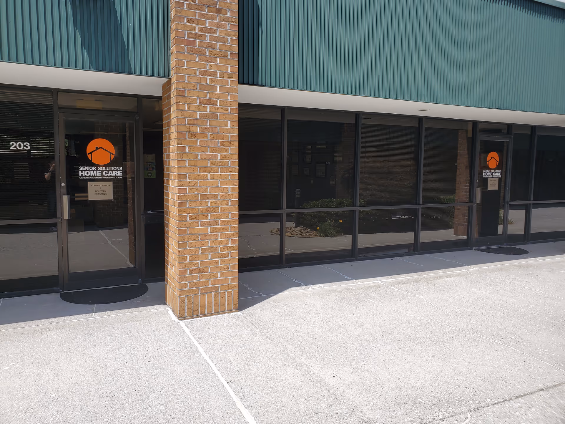Exterior entrance of Senior Solutions Home Care with glass doors and brick column.