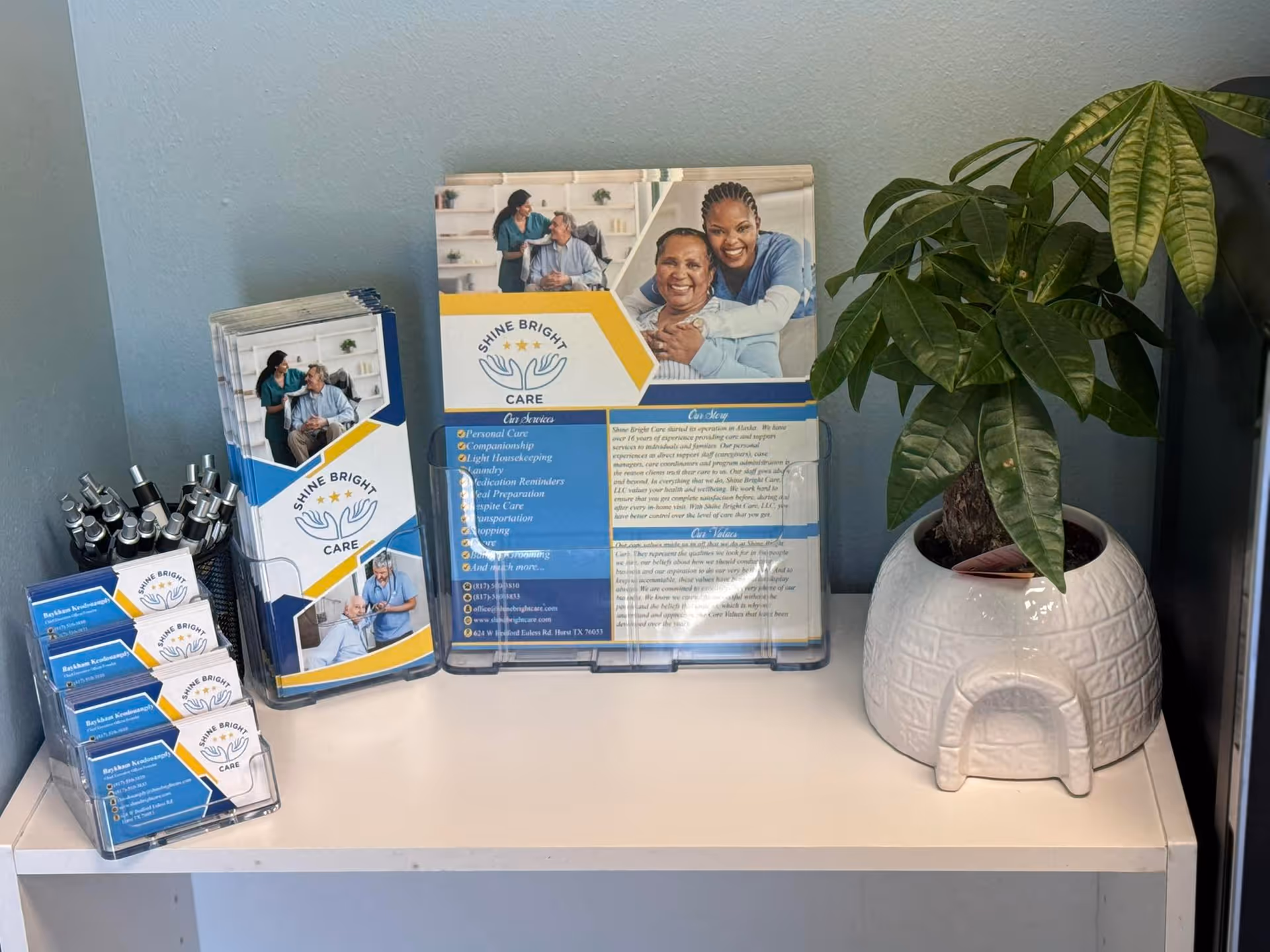 Shine Bright Care brochures and a potted plant on a white counter indoors.