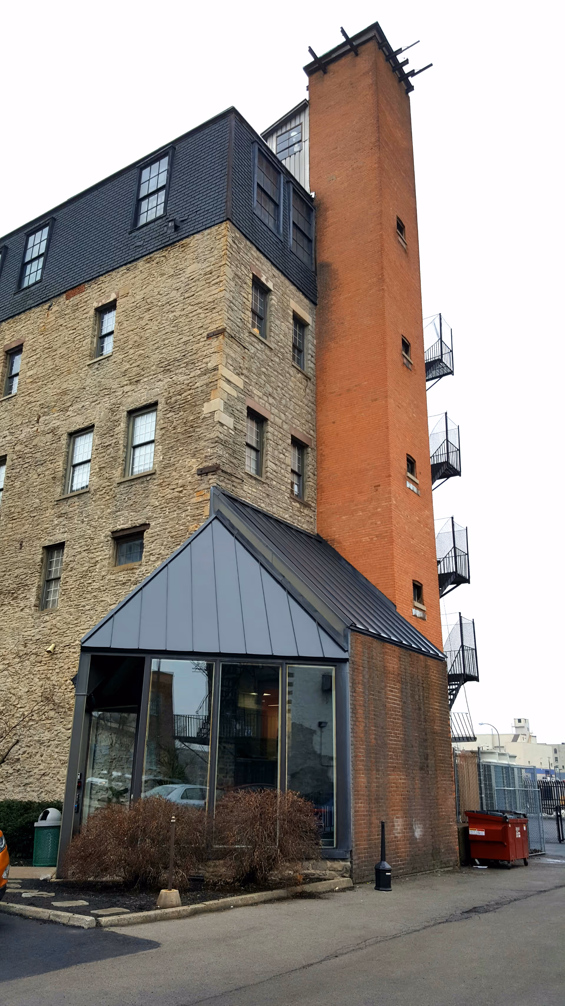 Brick multi-story building with glass entry and fire escapes along a tall orange tower.