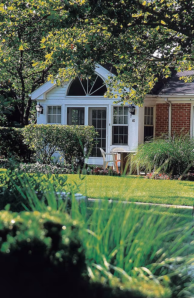 Front exterior view of a residence with a small porch, chairs, and lush landscaping.