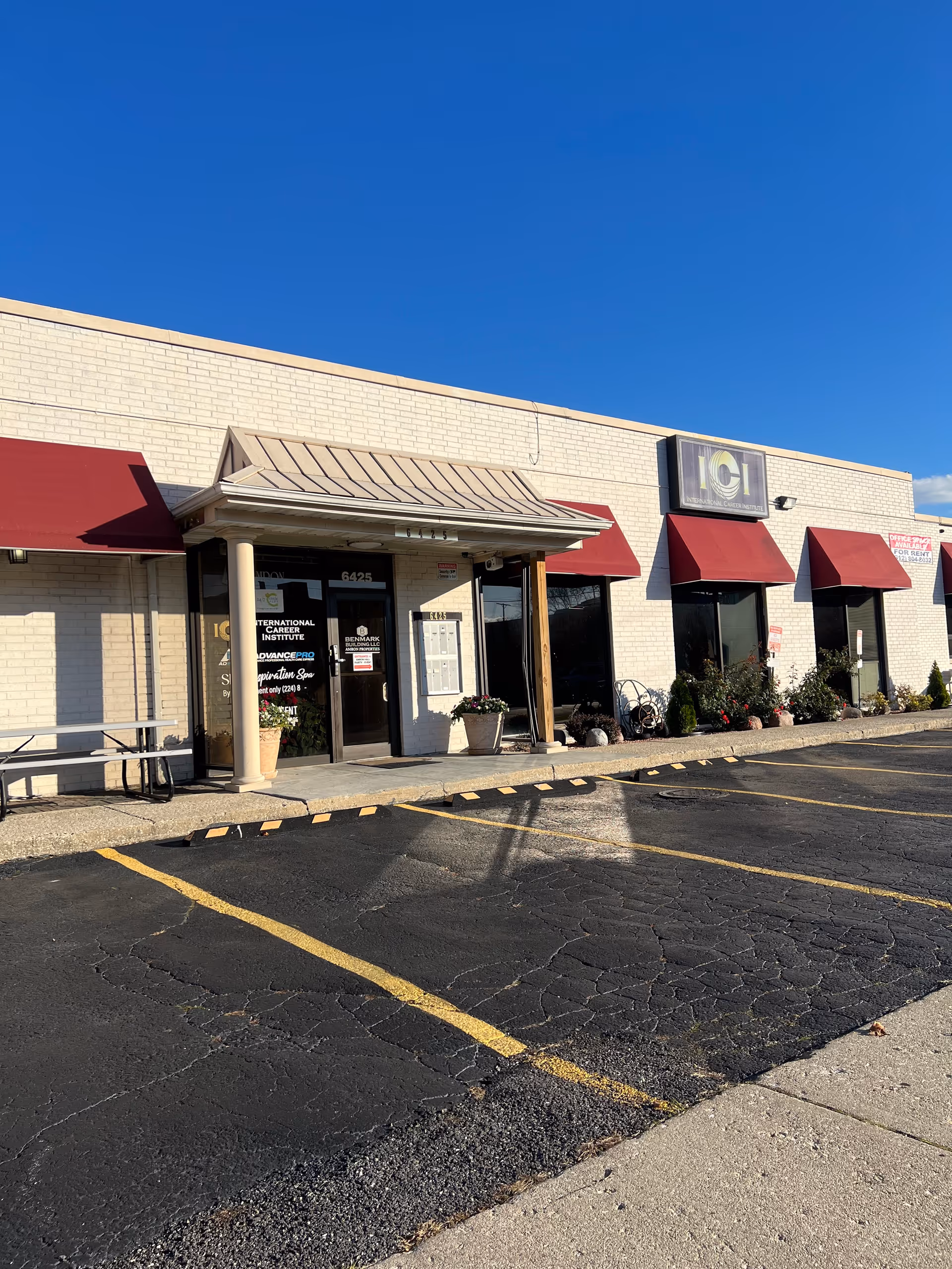 Exterior view of a low-rise retail strip with red awnings and a parking lot.
