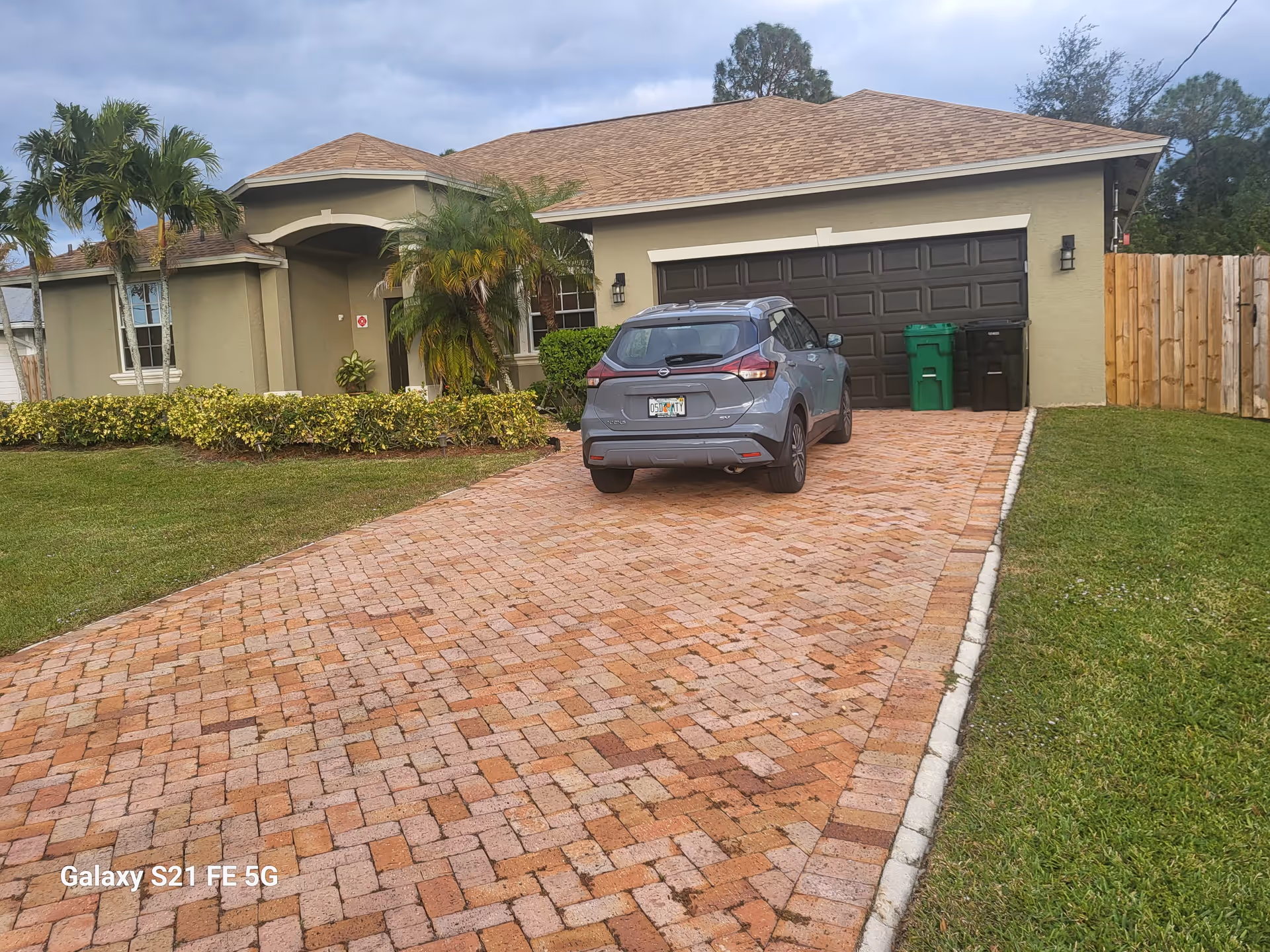 Residential-style building with brick driveway, parked SUV, and a two-car garage.