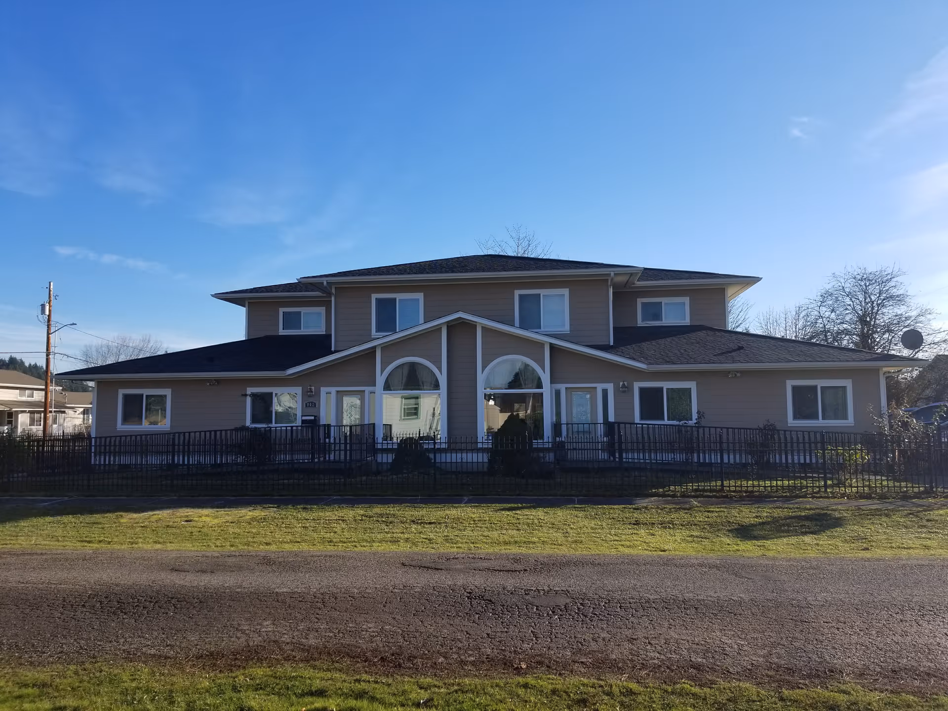 A two story senior living facility with a tan exterior, front arches, and a black fence.