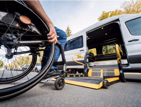 Wheelchair near a van with a lowered ramp in a parking lot.
