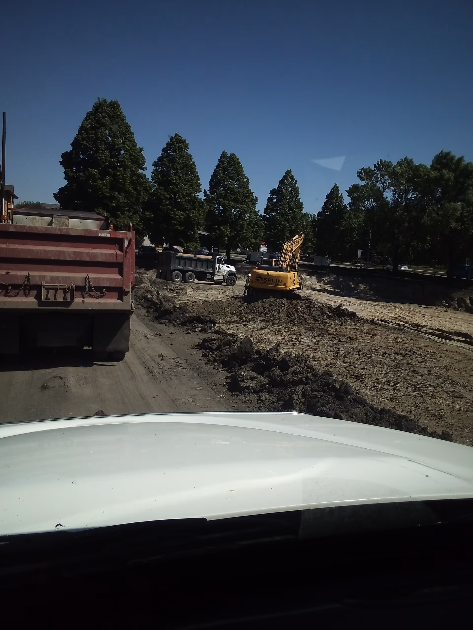 Outdoor construction site with excavator, dump truck, and dirt piles.