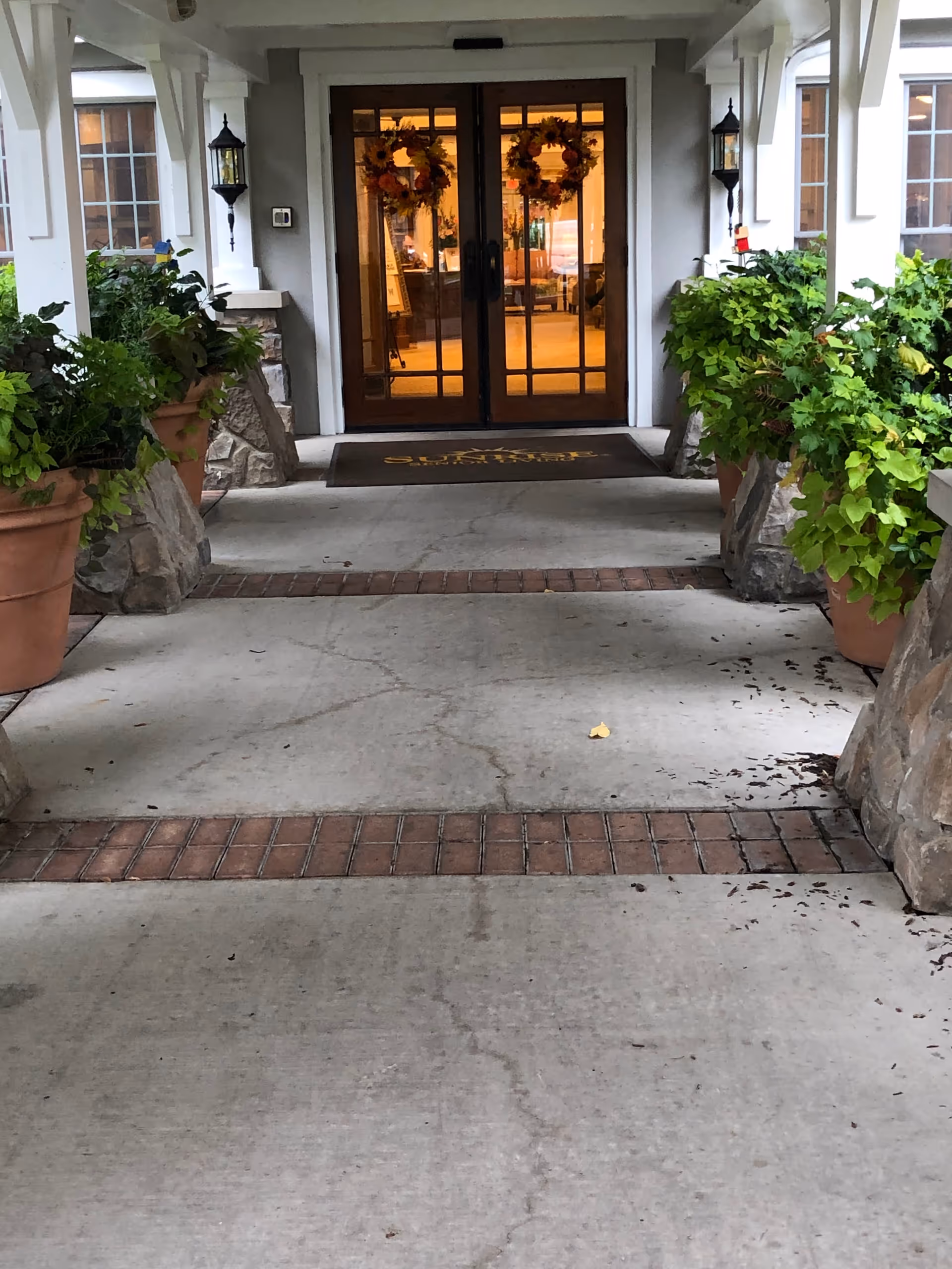 Exterior entrance of Sunrise on Hillcrest with glass doors, wreaths, and potted plants.