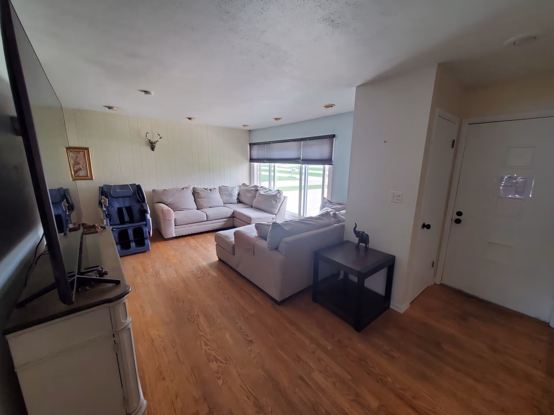 A cozy living room with beige sectionals, a mounted deer head, TV, and wooden floors.