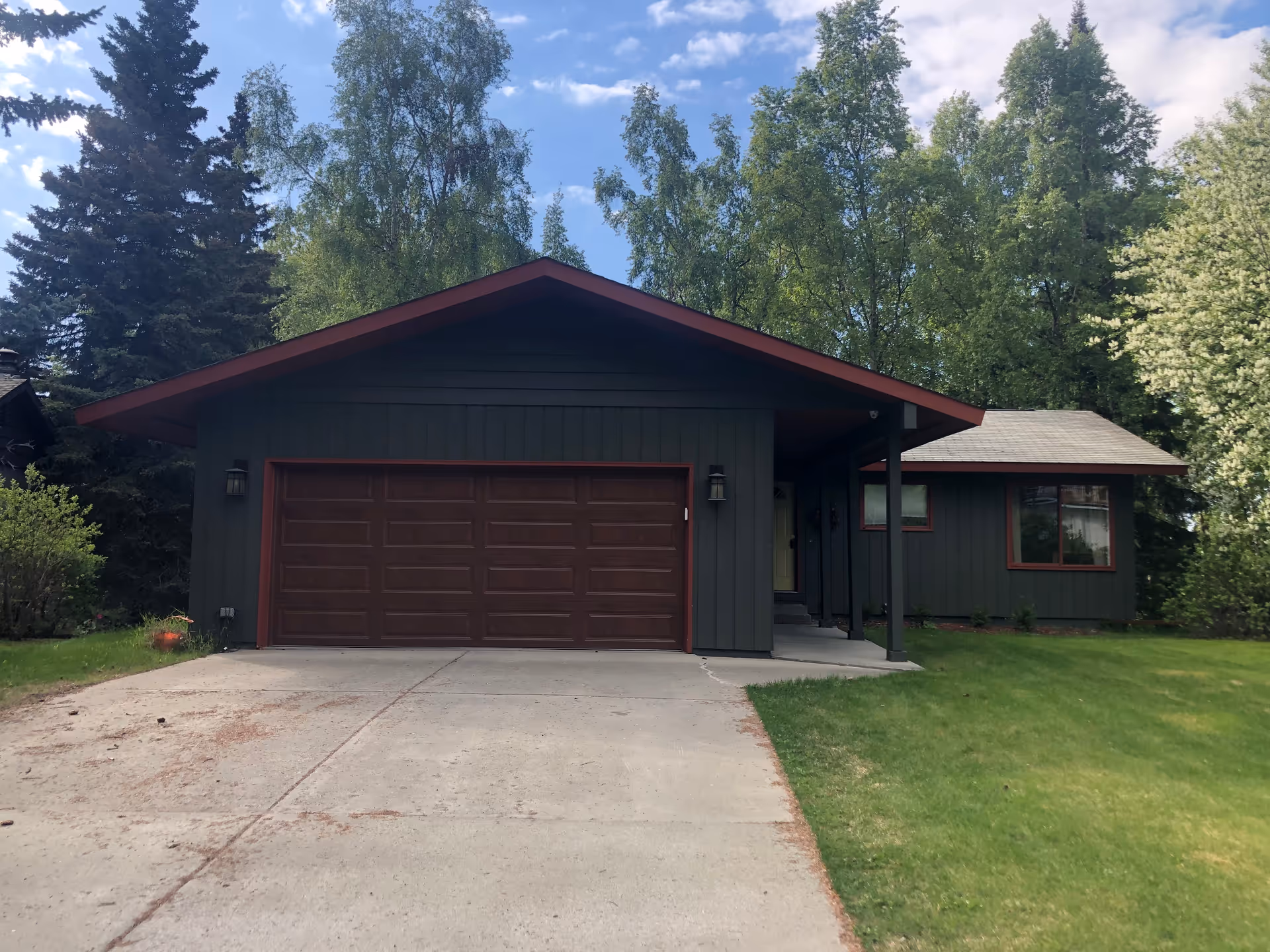 Modern single-story house with dark gray siding, red trim, and attached garage on a grassy lawn.