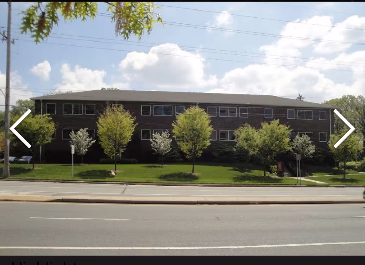 Two-story brick senior care building with trees and a grassy front yard along a street