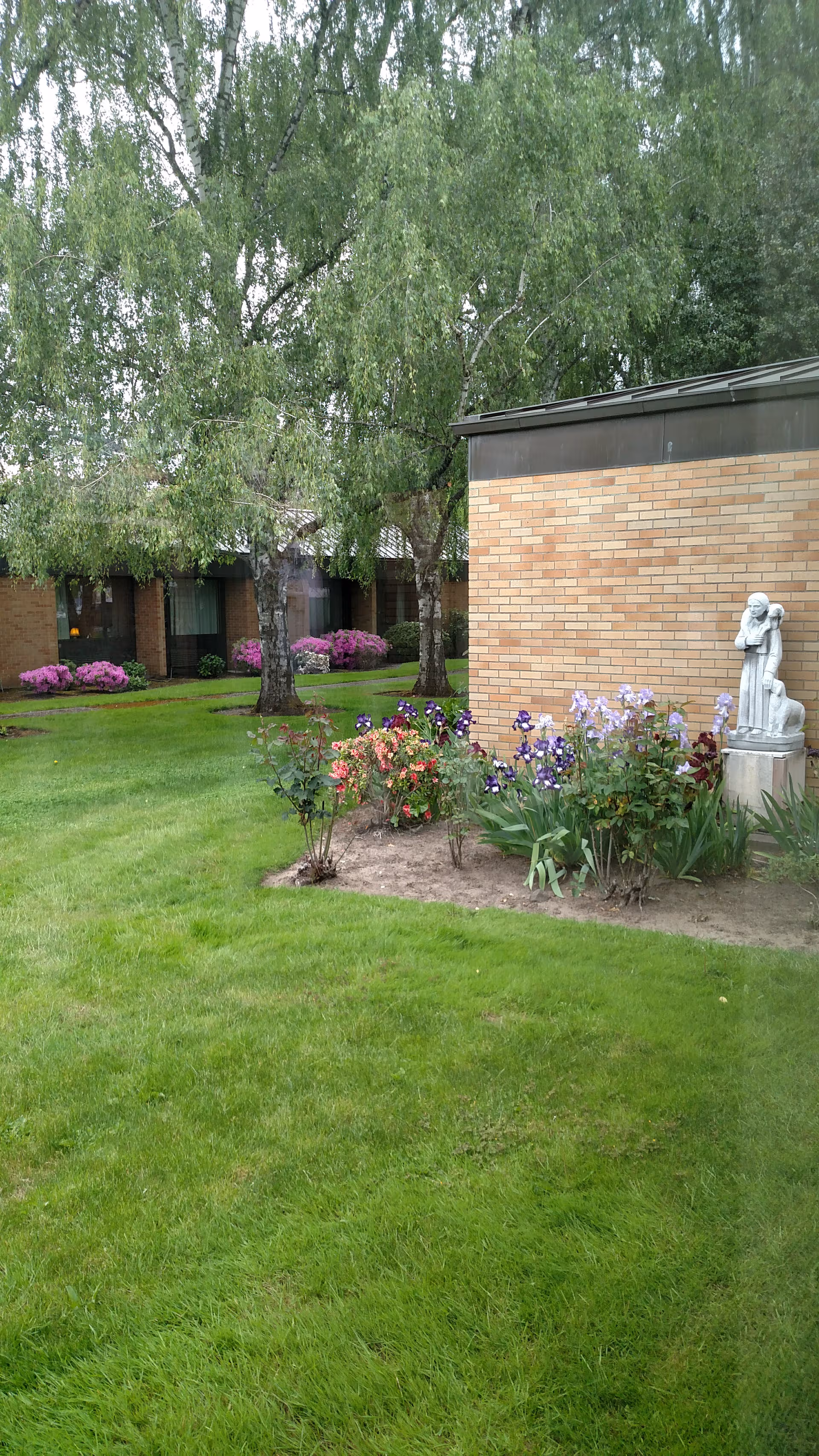 Well-kept outdoor garden with blooming flowers and a statue beside a brick building.