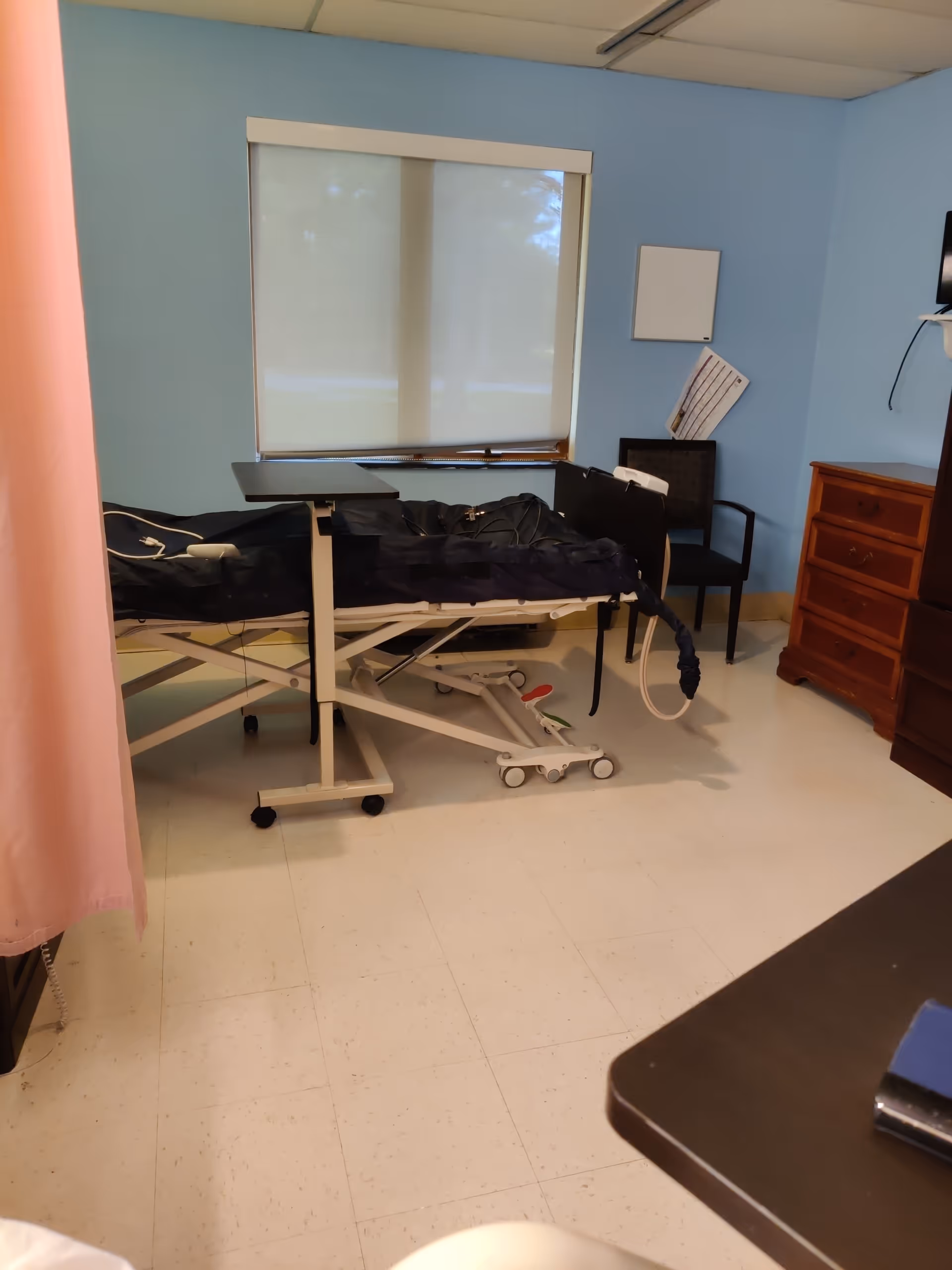 A hospital-style patient bed on a mobile frame in a blue-walled room.