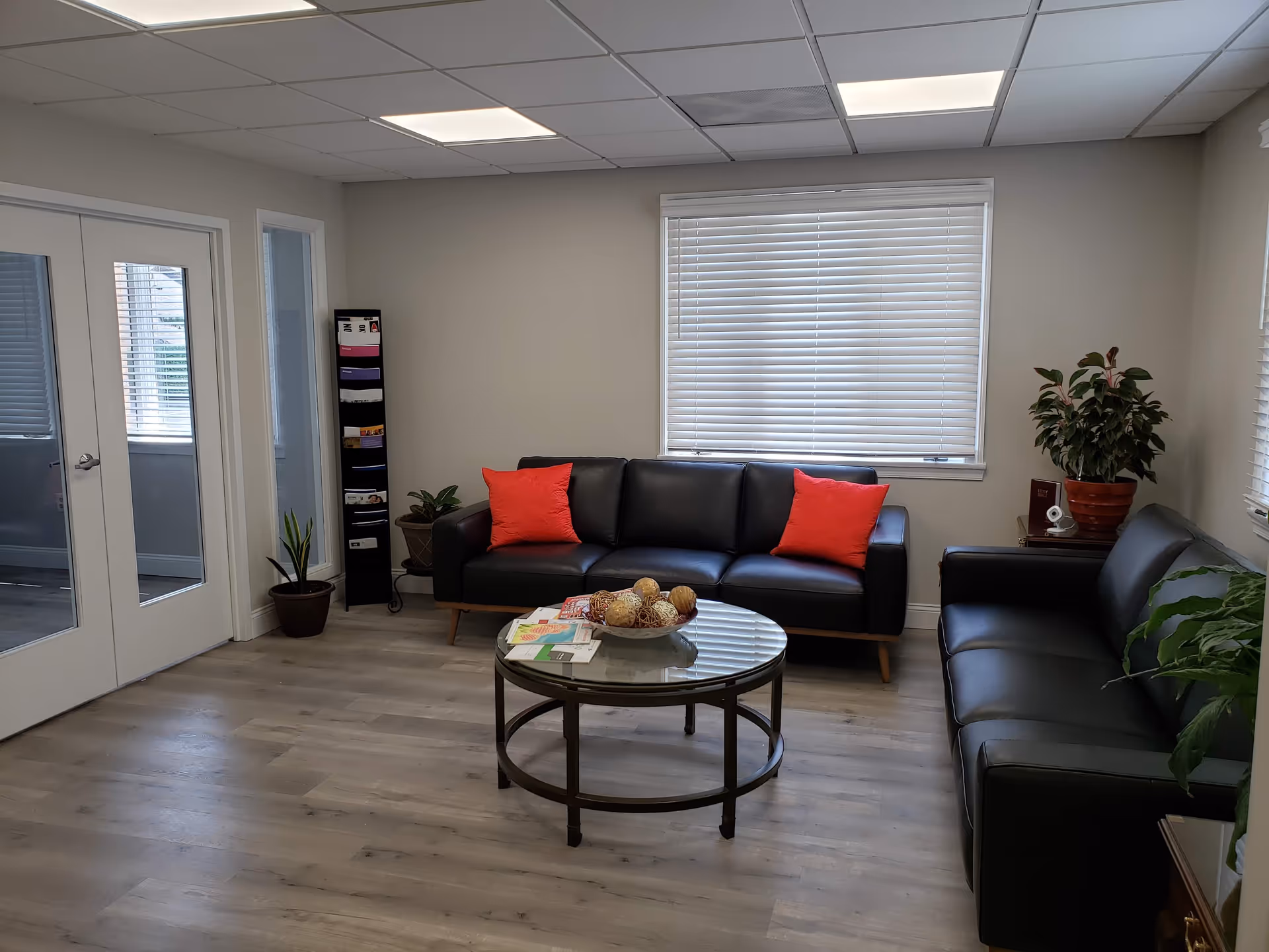 Modern lounge area with black sofas, red cushions, glass coffee table, and potted plants.