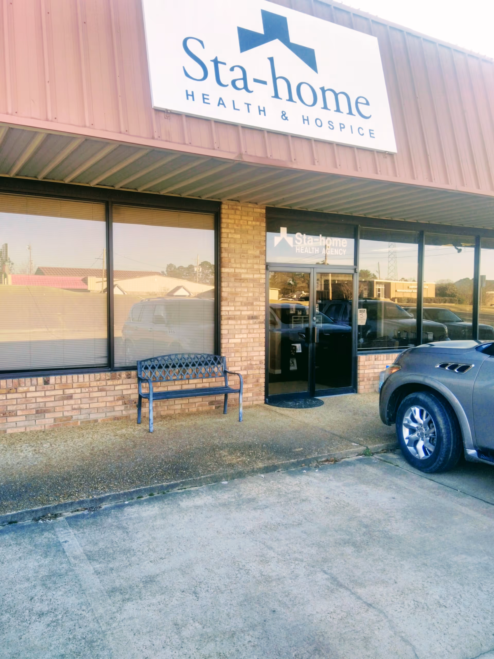 Exterior view of Sta-Home Health & Hospice storefront with bench and parked car