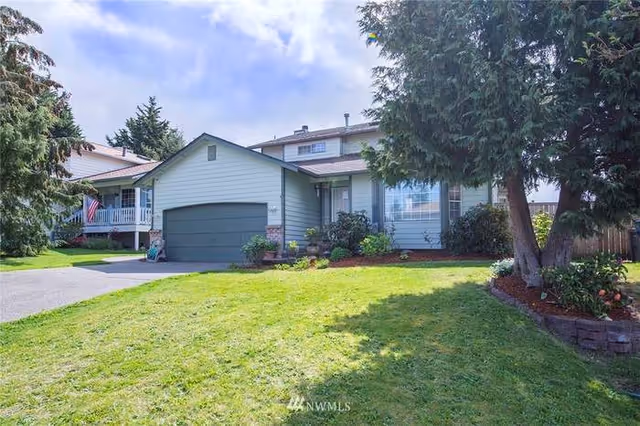Front view of a two-story suburban house with an attached garage, lawn, and mature trees.