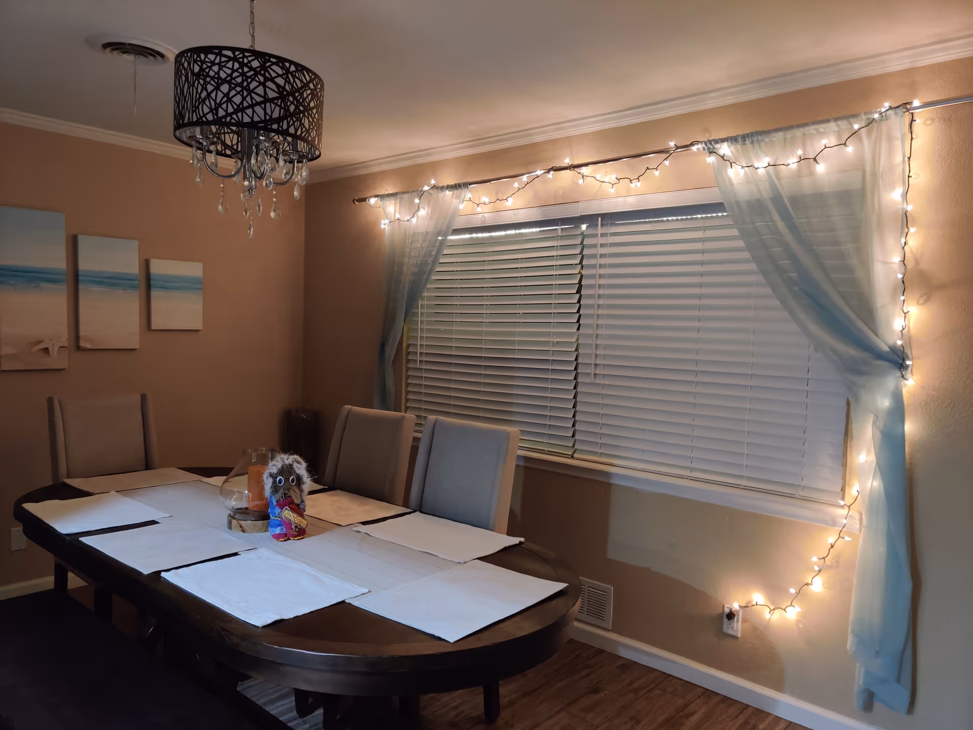 Dining room with long table, placemats, string lights, blue curtains, and chairs.