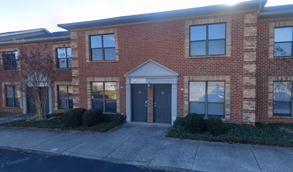 Brick senior living facility exterior with a central double-door entrance and trimmed shrubs