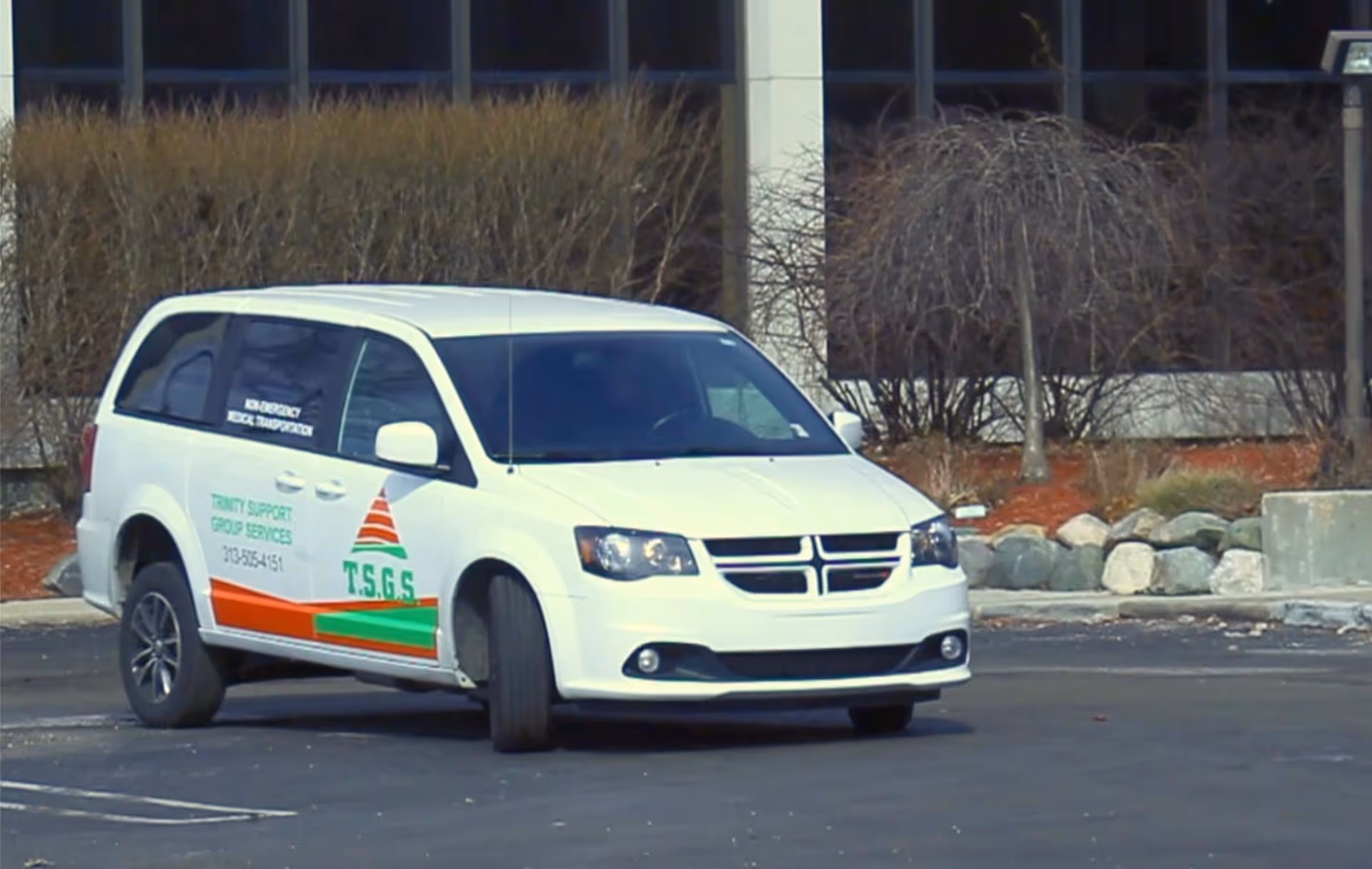 White van labeled Trinity Support Group Services parked in a lot outside a building.