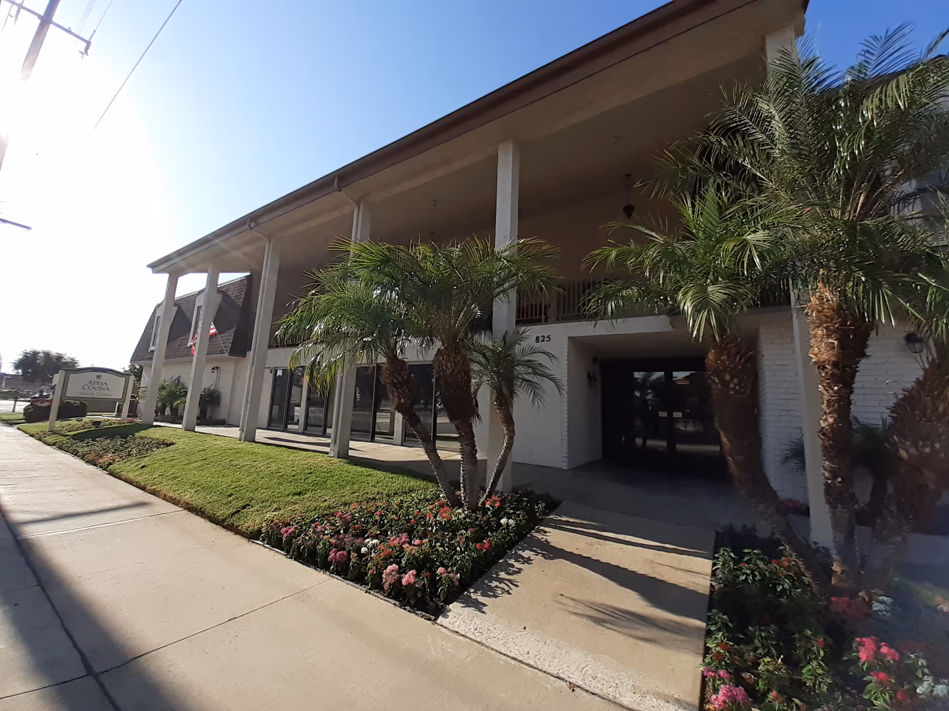 Exterior view of Atria Covina with entrance, palm trees, and landscaped walkway.