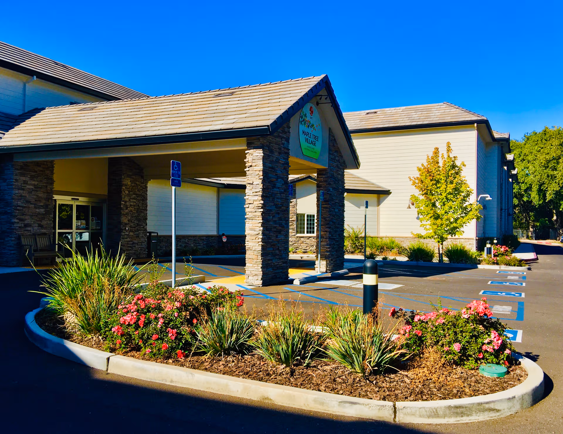Front entrance of ACC Maple Tree Village senior living facility with stone columns and landscaping.