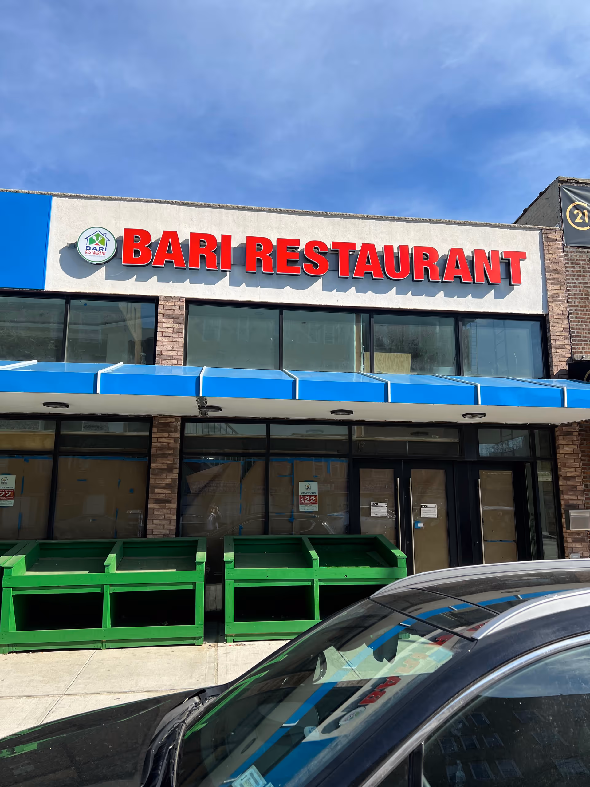 Exterior storefront with a large red Bari Restaurant sign, green dumpsters, and a parked car.