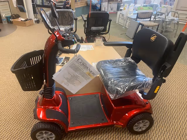 Red mobility scooter on display inside a senior living showroom with seating.