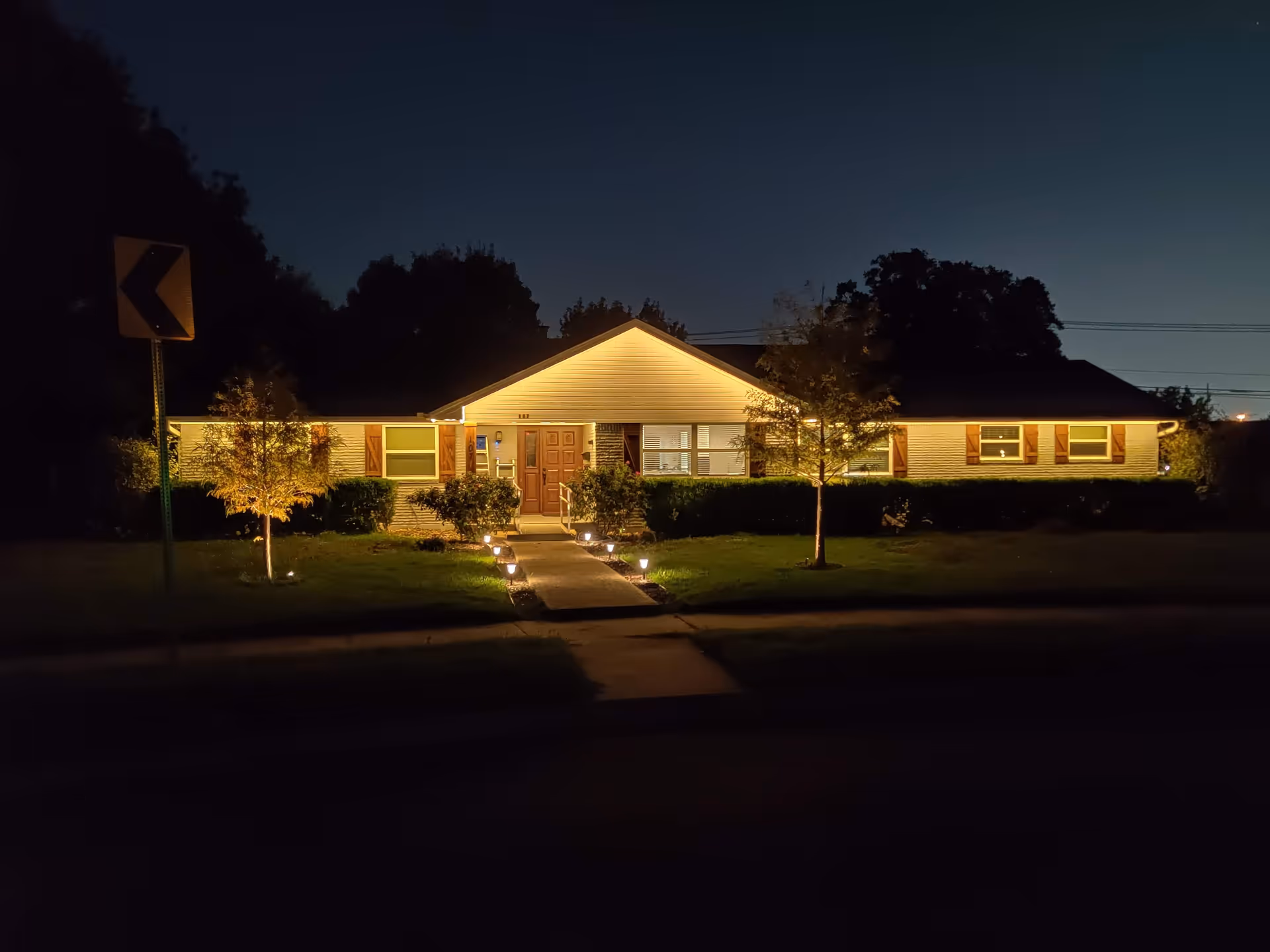 Night view of a single-story assisted living facility with lit entry path.