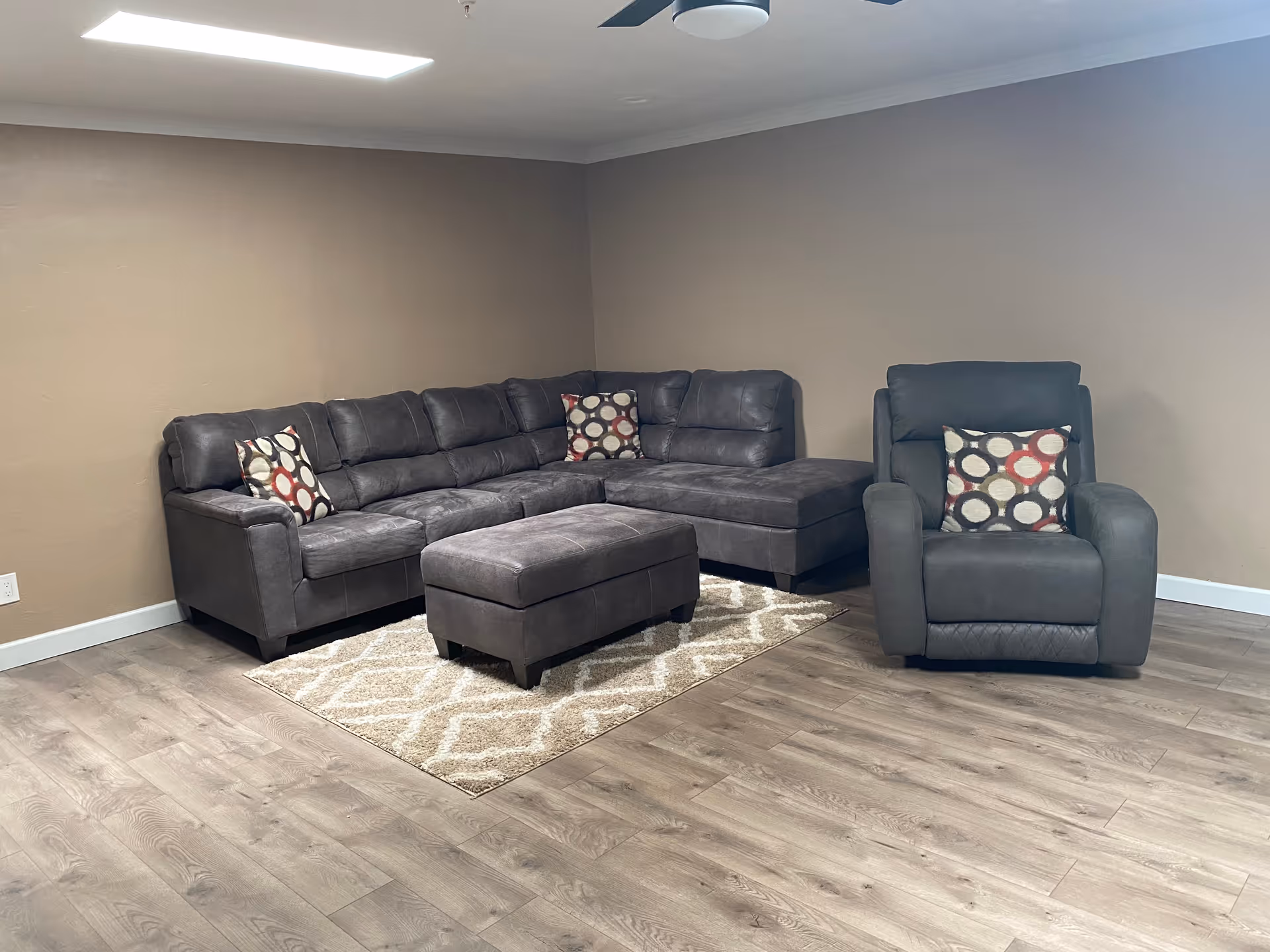 Grey sectional sofa with ottoman and armchair in a cozy living room setting with patterned cushions.