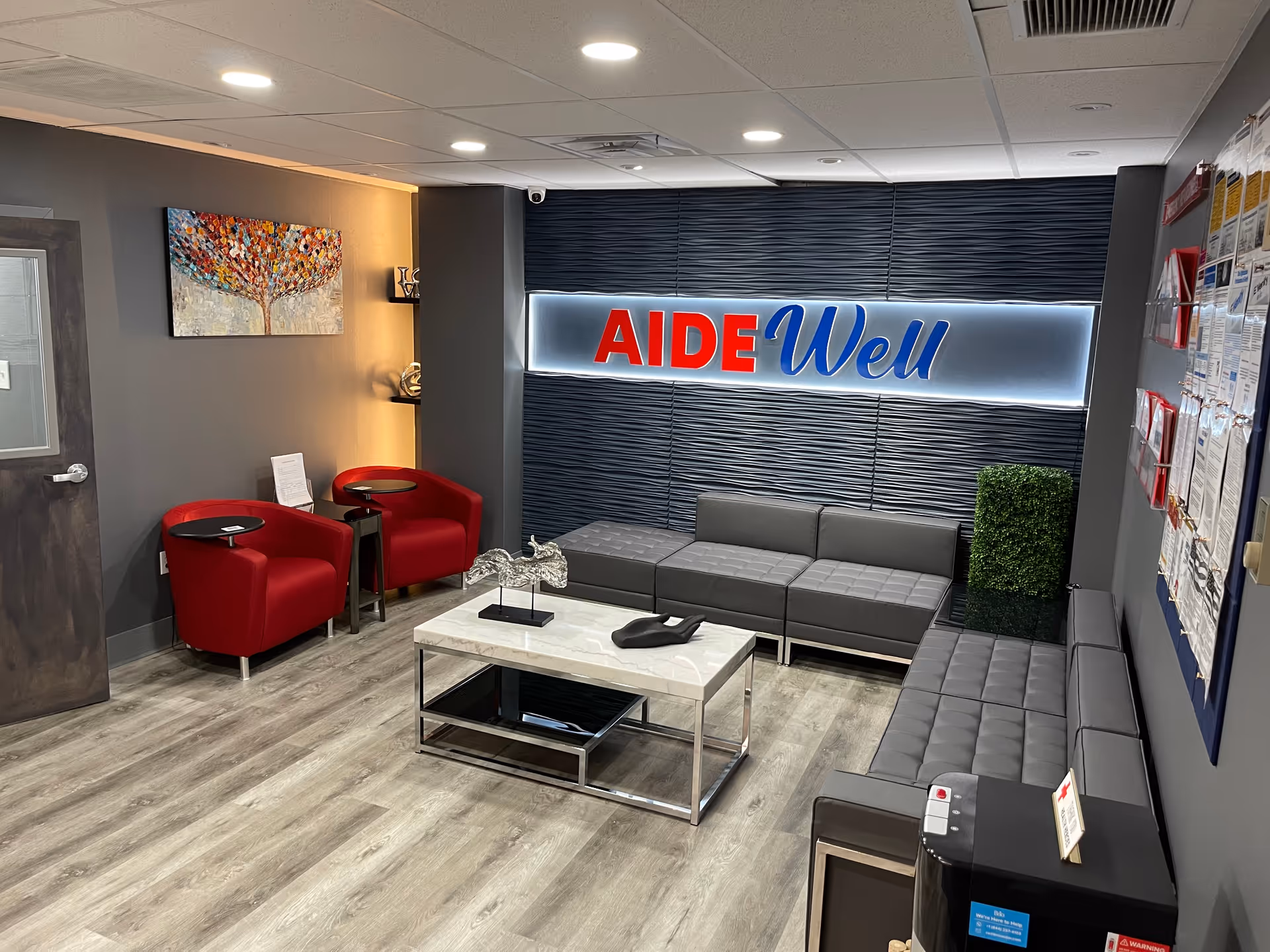Modern facility lobby with gray seating, red chairs, and illuminated AIDEWell sign.