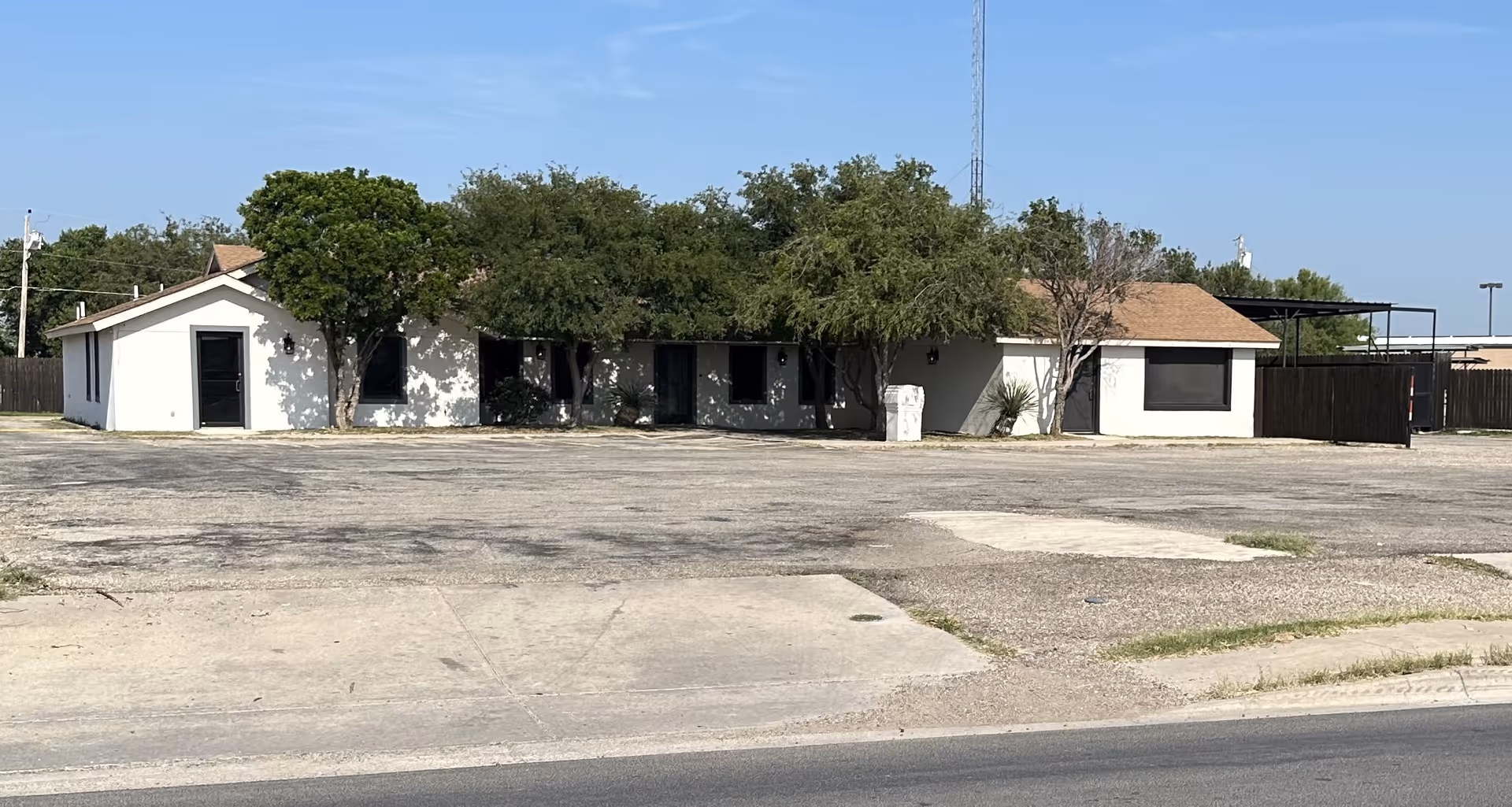 Front view of a single-story white facility with trees and a parking lot.