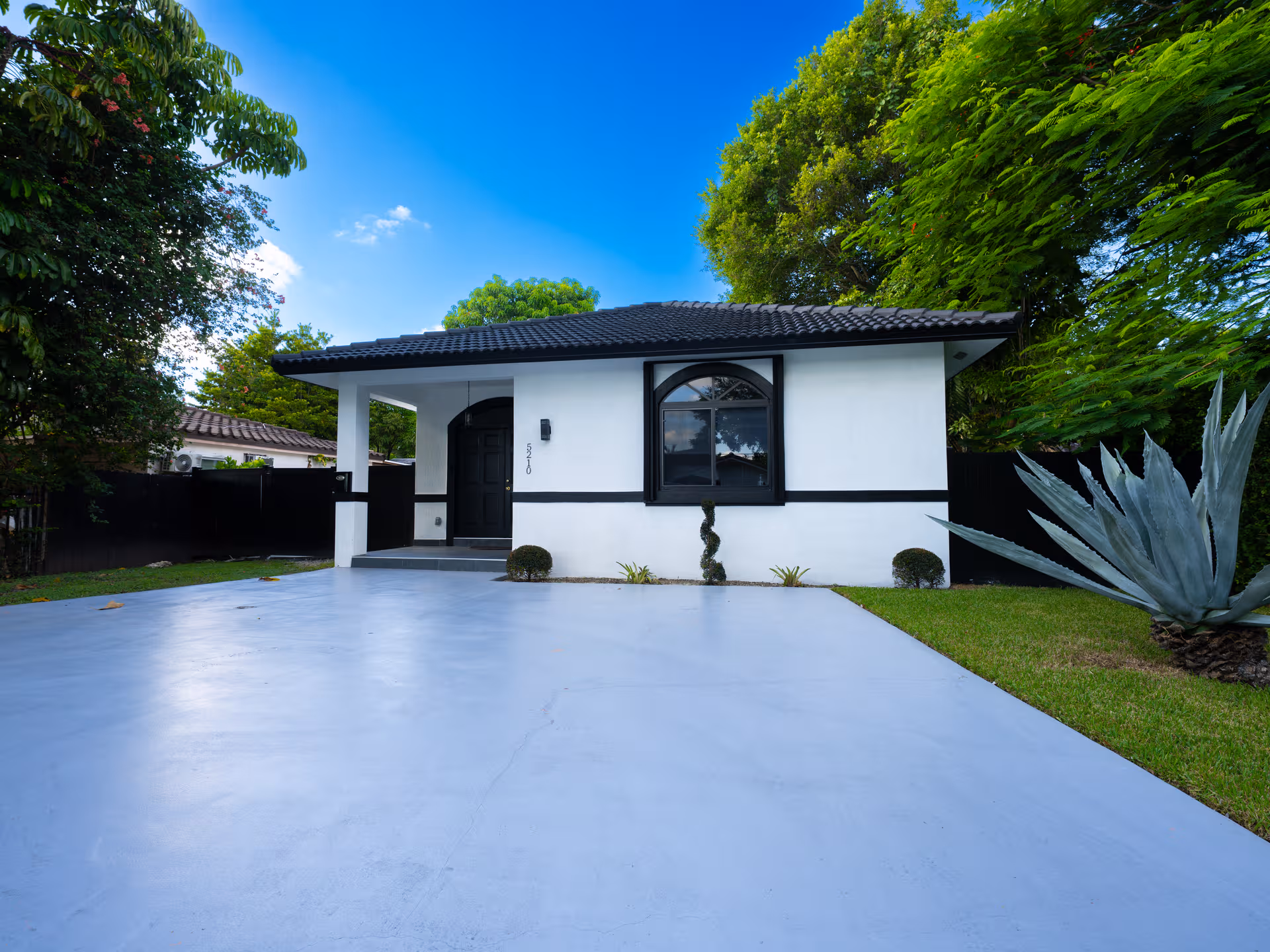 A white, single-story building with black trim sits at the end of a blue driveway.