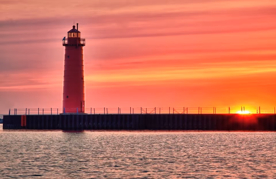 Sunset over a red lighthouse on a breakwater with calm water.