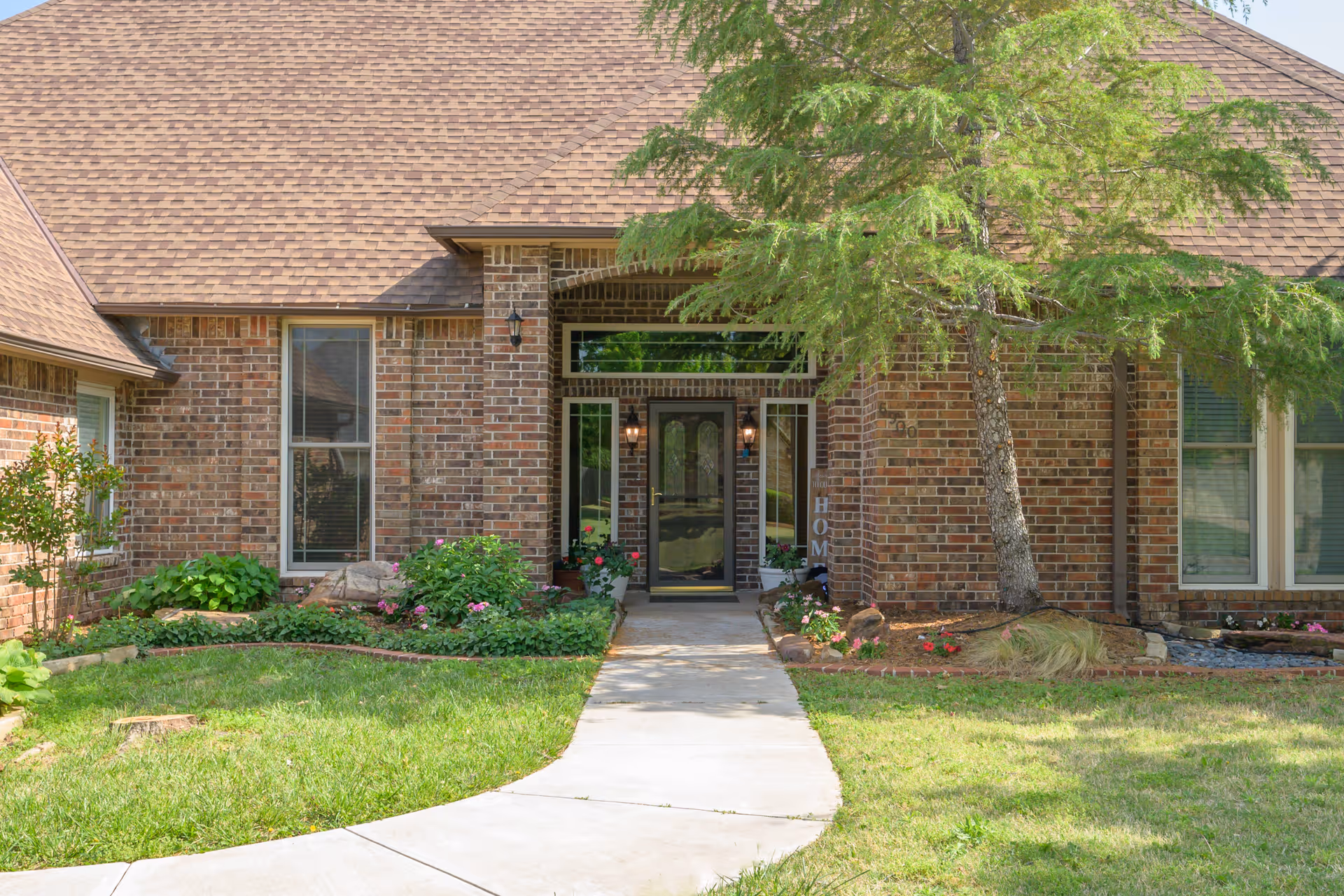 Brick senior living facility entrance with glass doors, landscaped walkway, and trees.