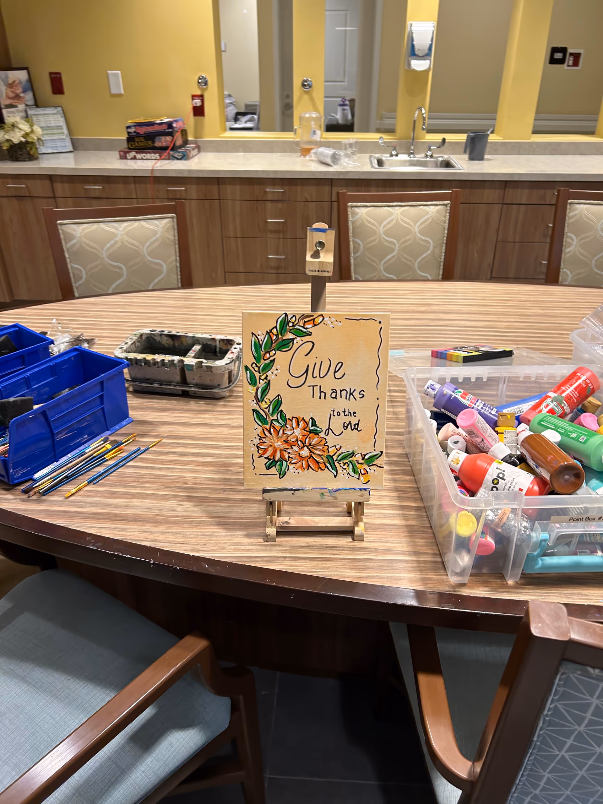 Craft table with art supplies and a 'Give Thanks' sign in a bright interior.