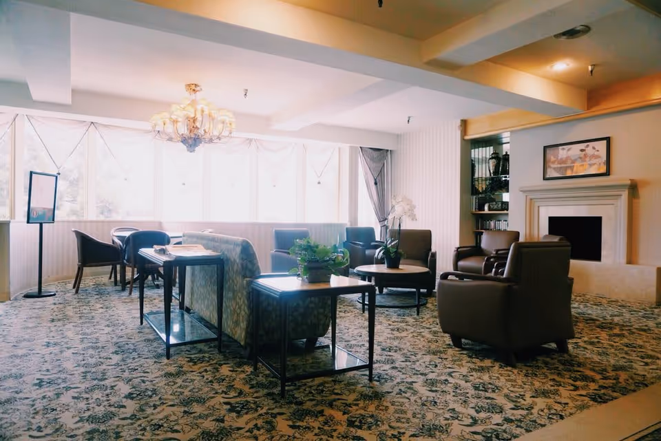 Sunlit common lounge with sofas, armchairs, tables, a chandelier and a fireplace.