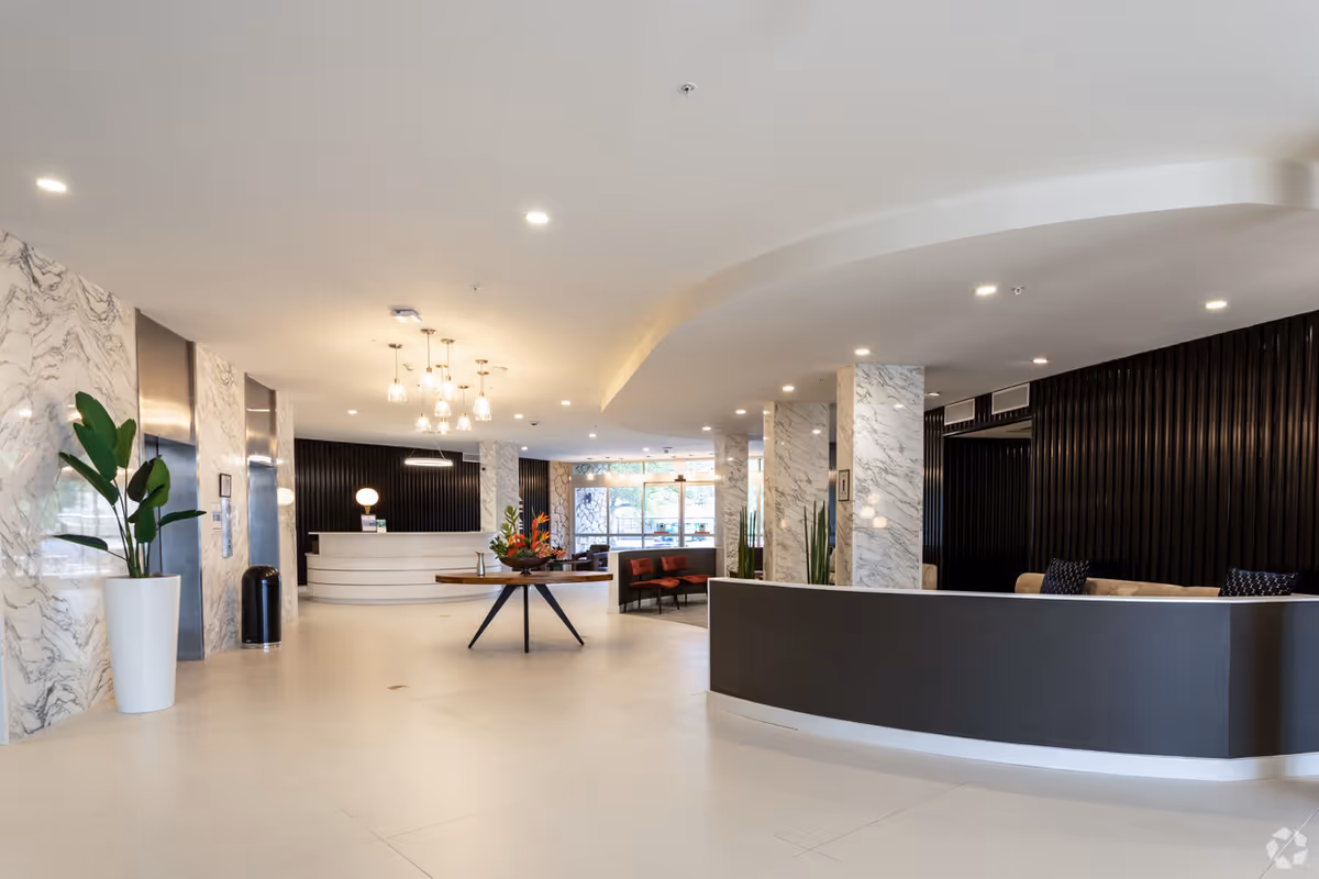 Bright modern senior living lobby with marble columns, curved reception desk, and seating area.