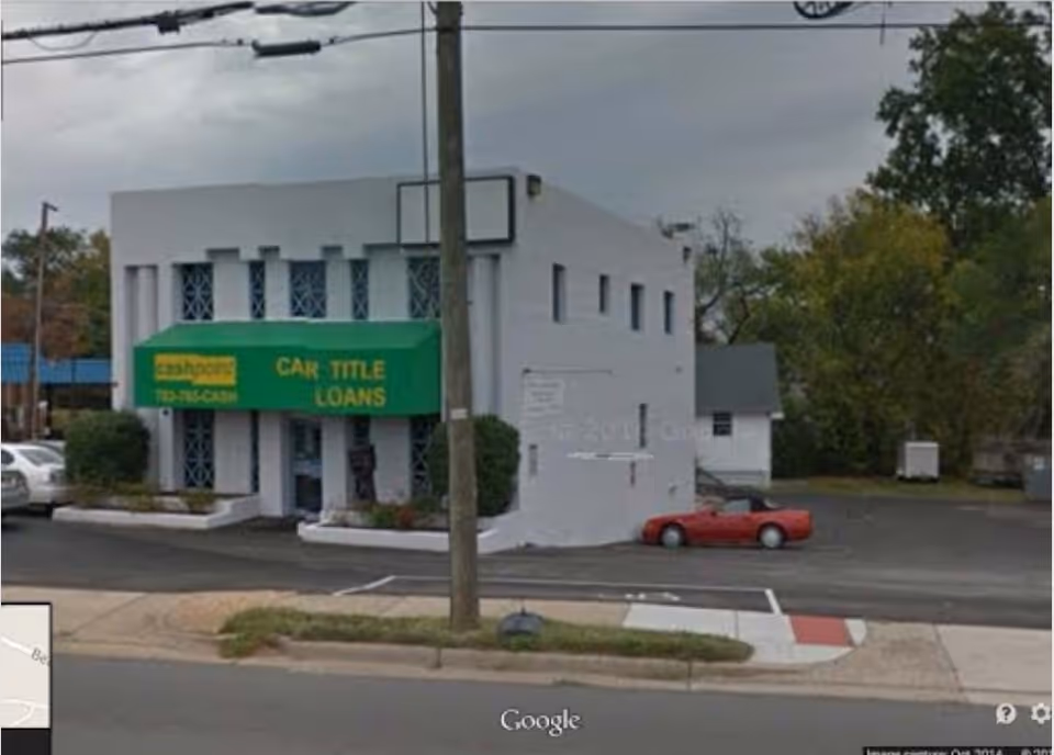 Two-story white storefront building with a bright green car-title-loans sign and parked cars.