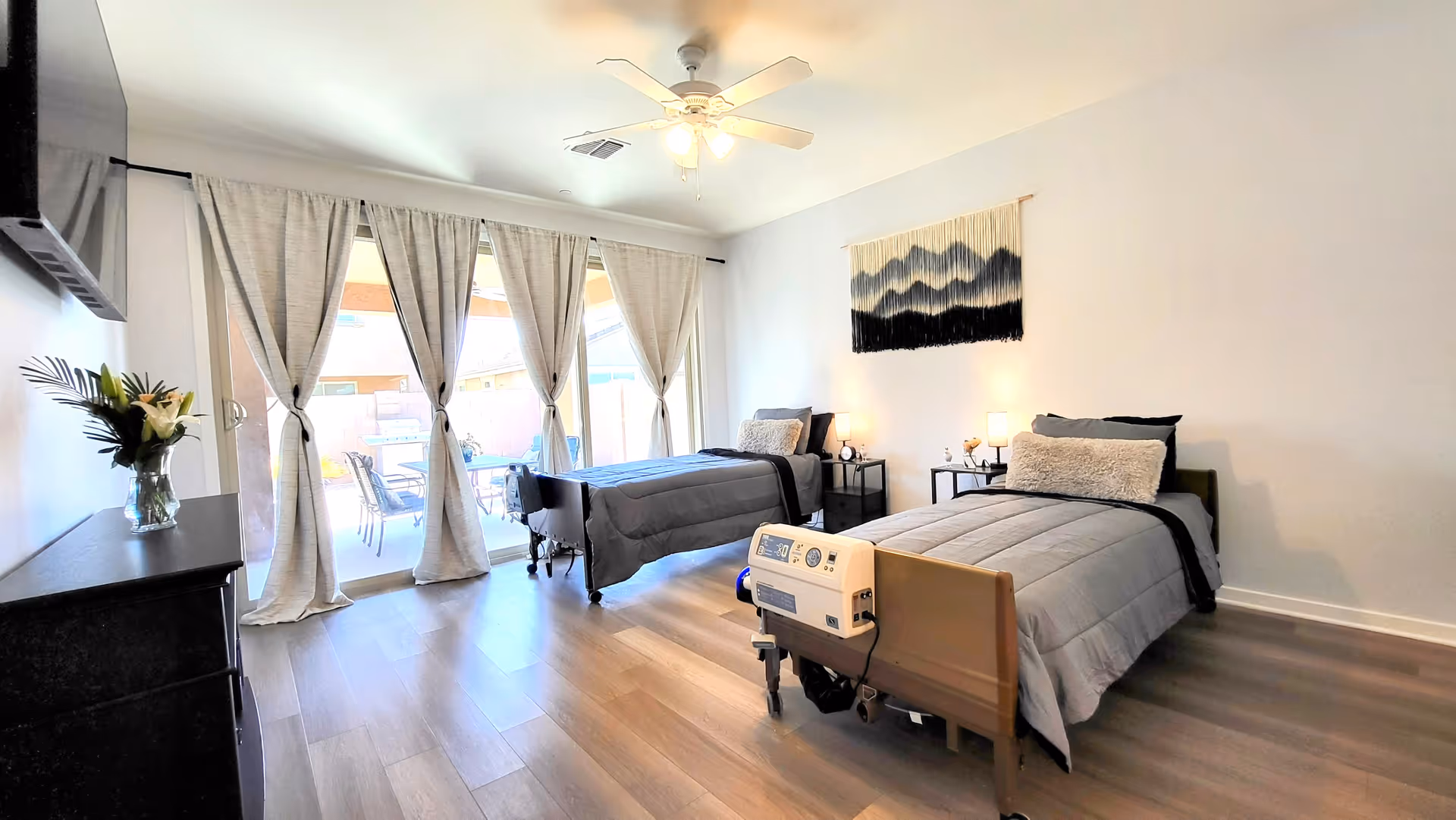 Bright, spacious patient room with two twin beds, a hospital bed, and doors opening to patio.