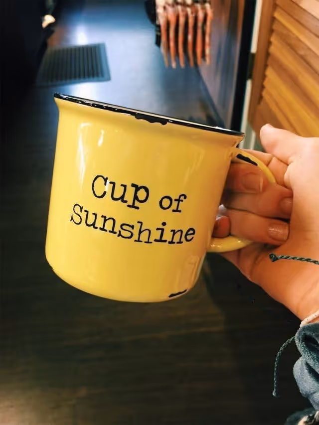 Yellow mug with 'Cup of Sunshine' held indoors