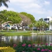 Lush outdoor landscape with a pond and modern building in the background.