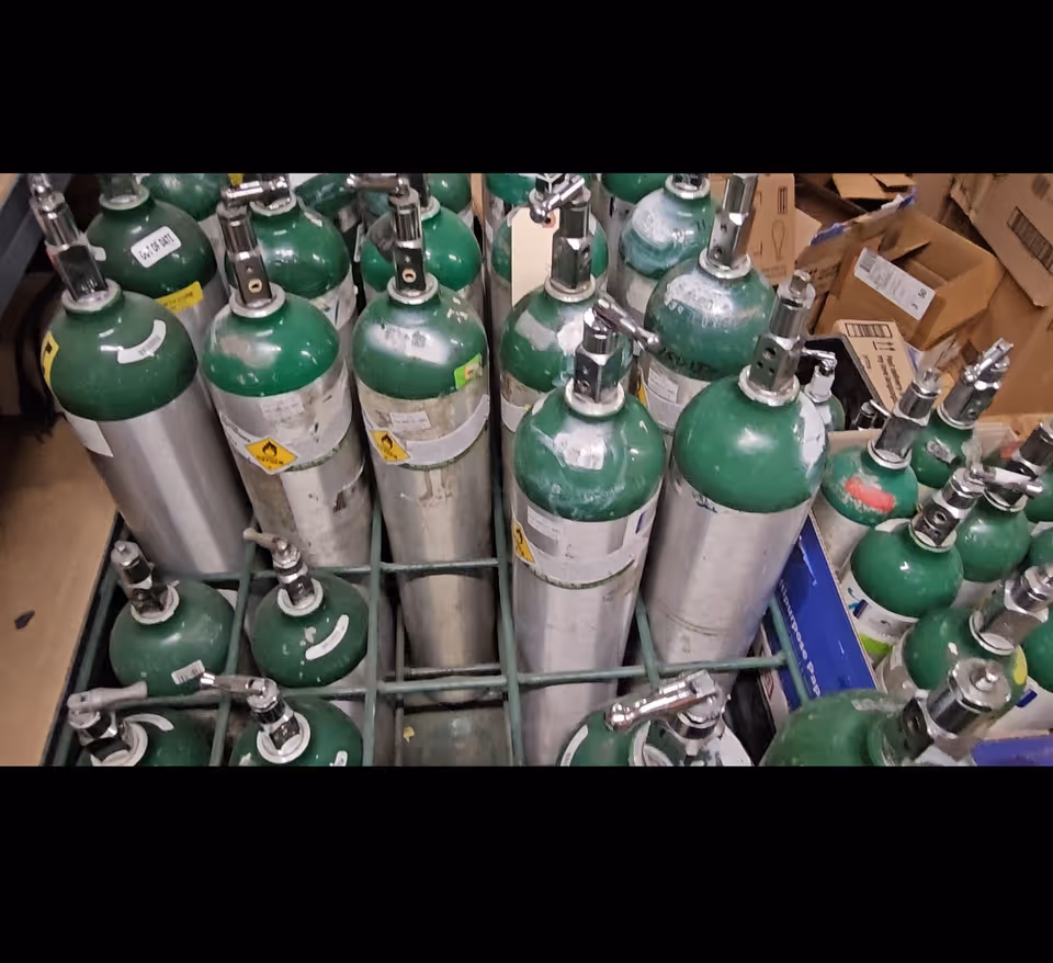 Storage room filled with stacked green and silver oxygen tanks and boxes.