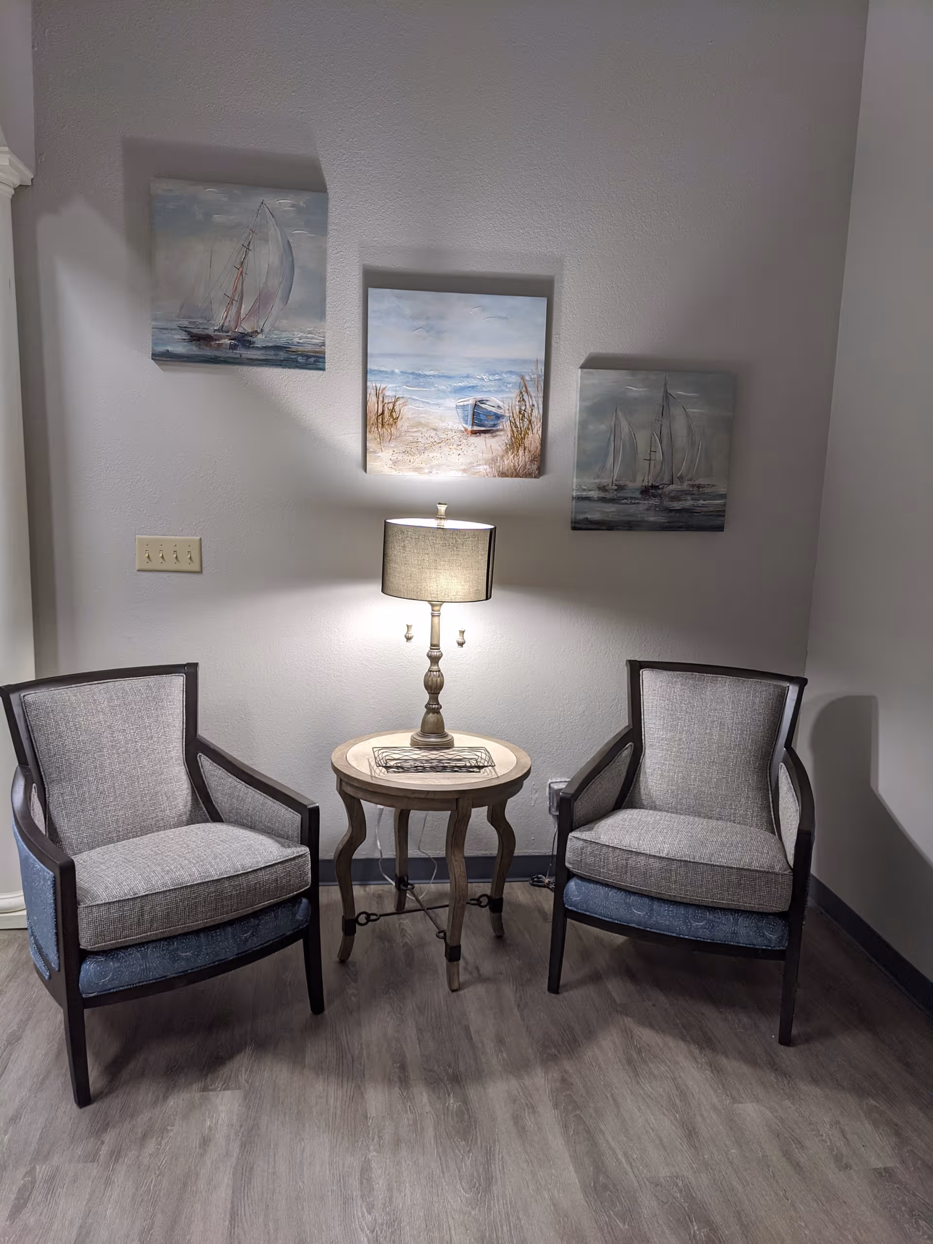 Two upholstered chairs flank a small round table with a lamp in a cozy lounge.