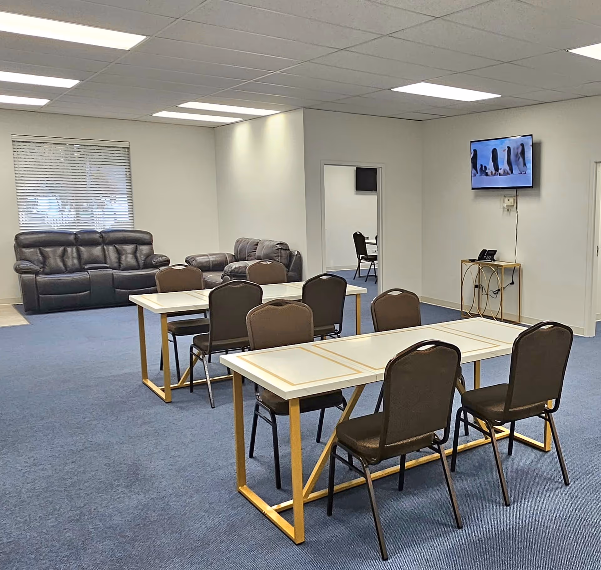 Interior common area with dining tables, chairs, sofas, and a wall-mounted TV.