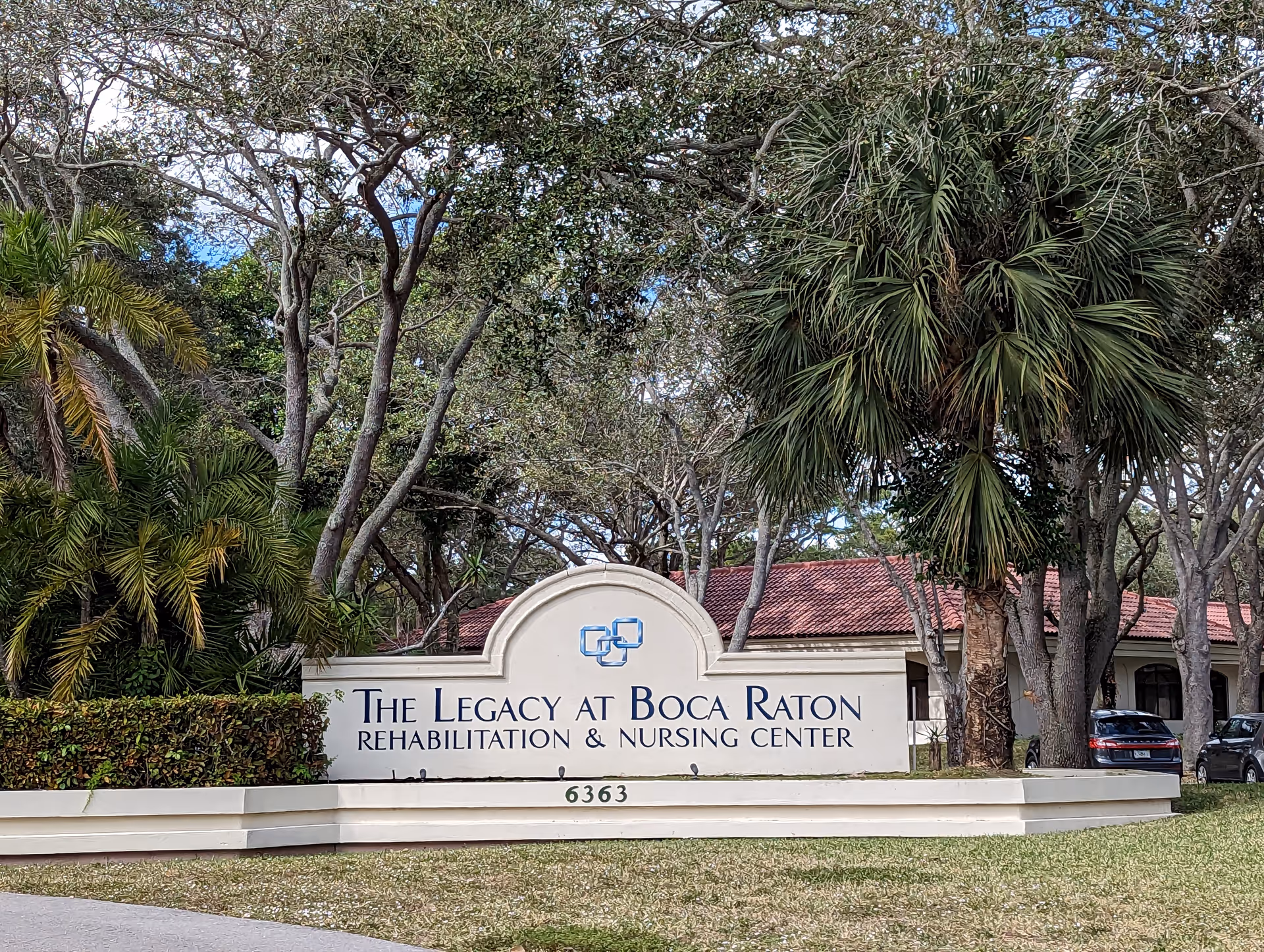 The Legacy at Boca Raton Rehabilitation & Nursing Center sign with trees and parked cars nearby.