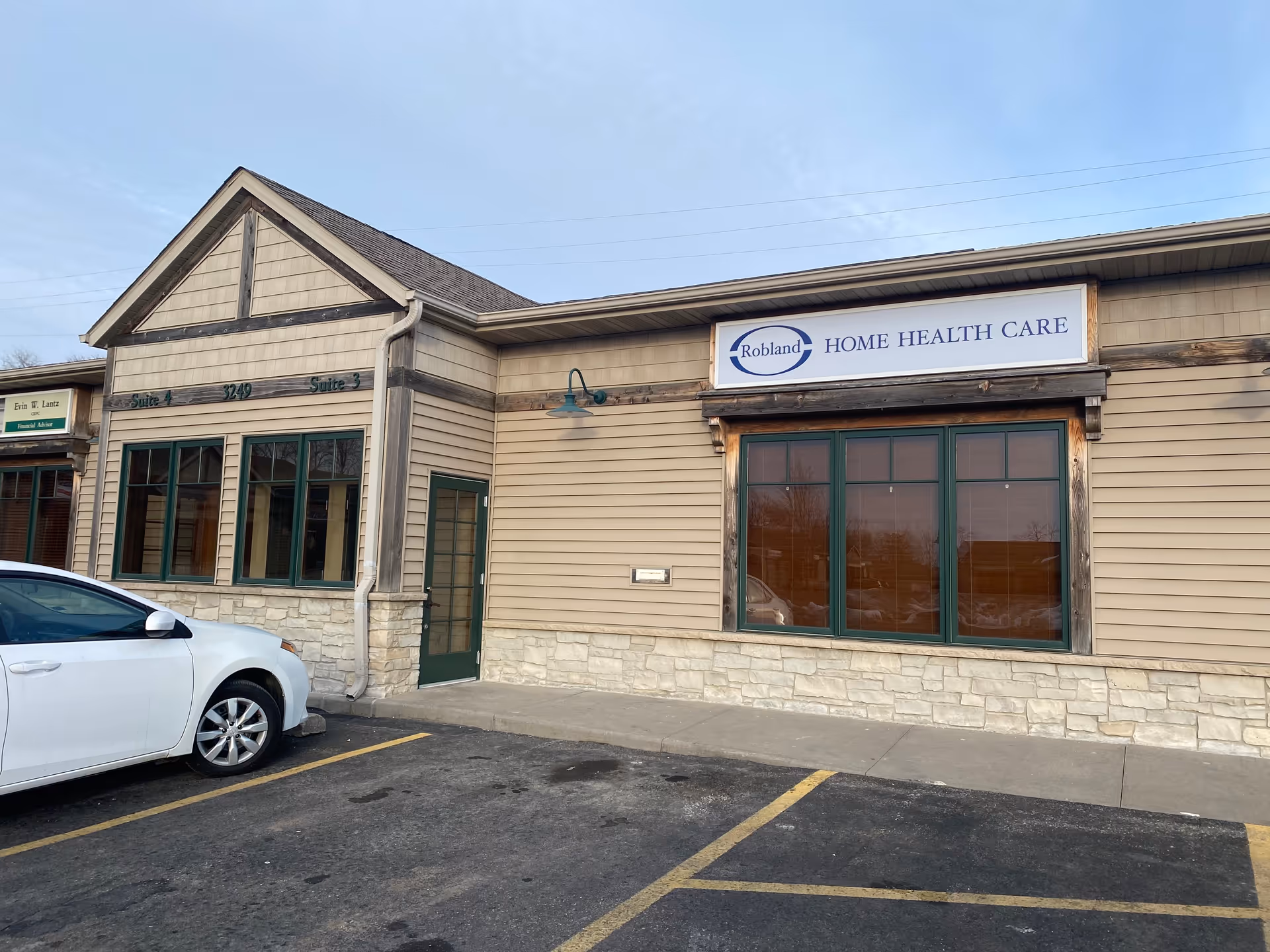 Exterior view of Robland Home Health Care building with sign and parked car in lot.
