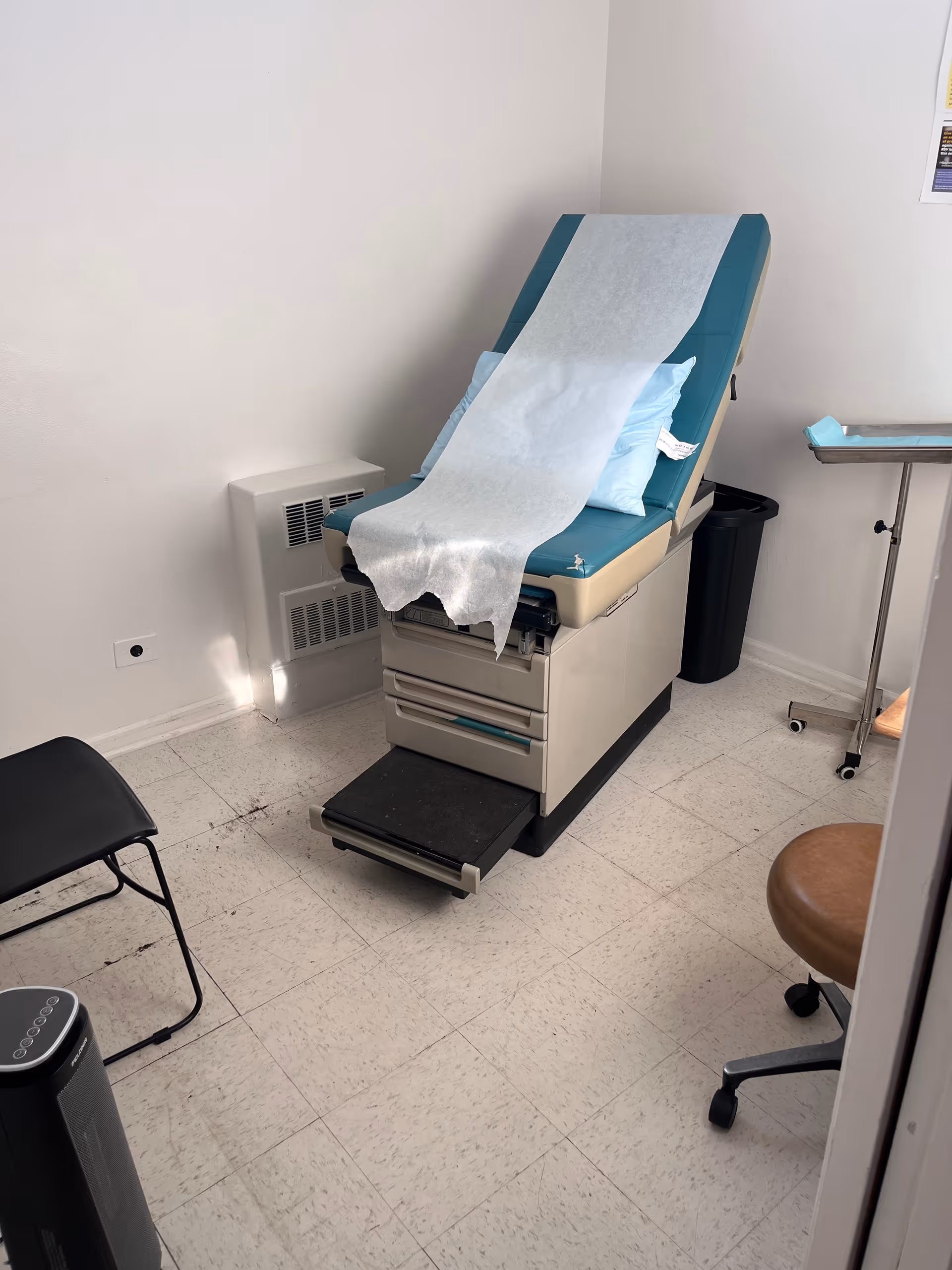 Medical examination chair with disposable paper, in a quiet clinic room with equipment.