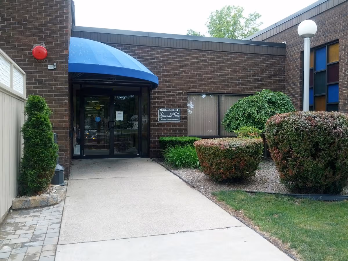 Brick building entrance to GrandeVille Senior Living Community with blue awning and glass doors.