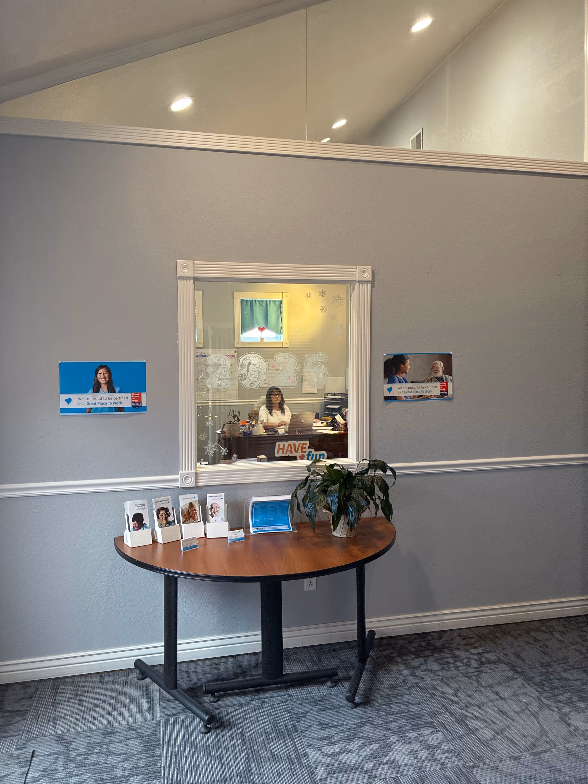 Reception area with window into a desk, brochures on a round table, and a plant.